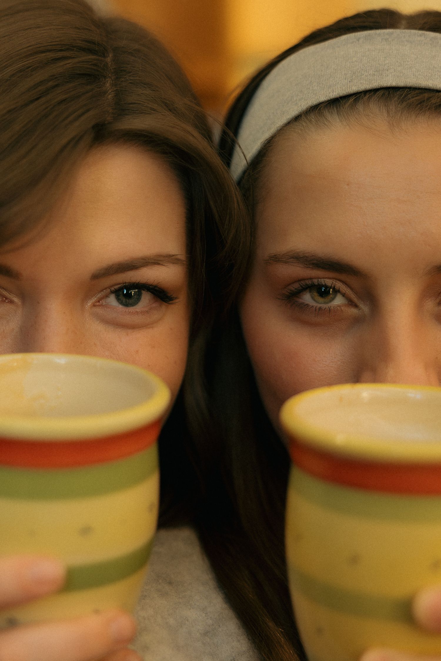 Close-up shot of two coffee cups held up in front of bookshelves.