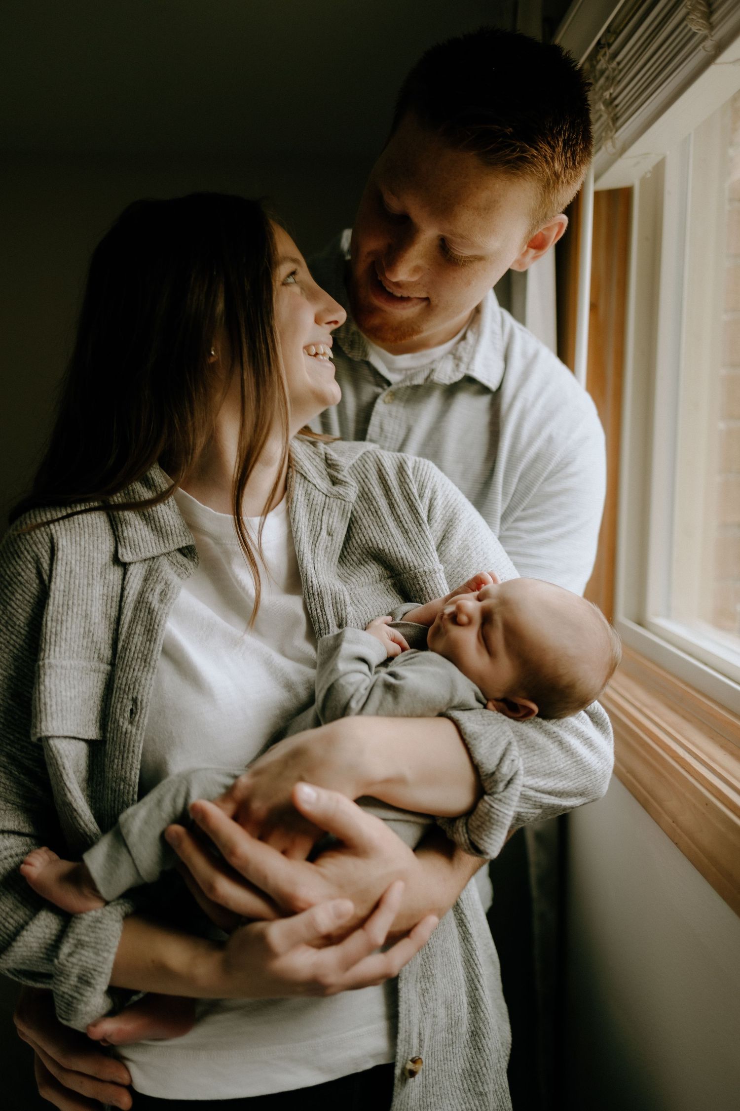 A tender family moment by a window as they cradle their newborn baby.