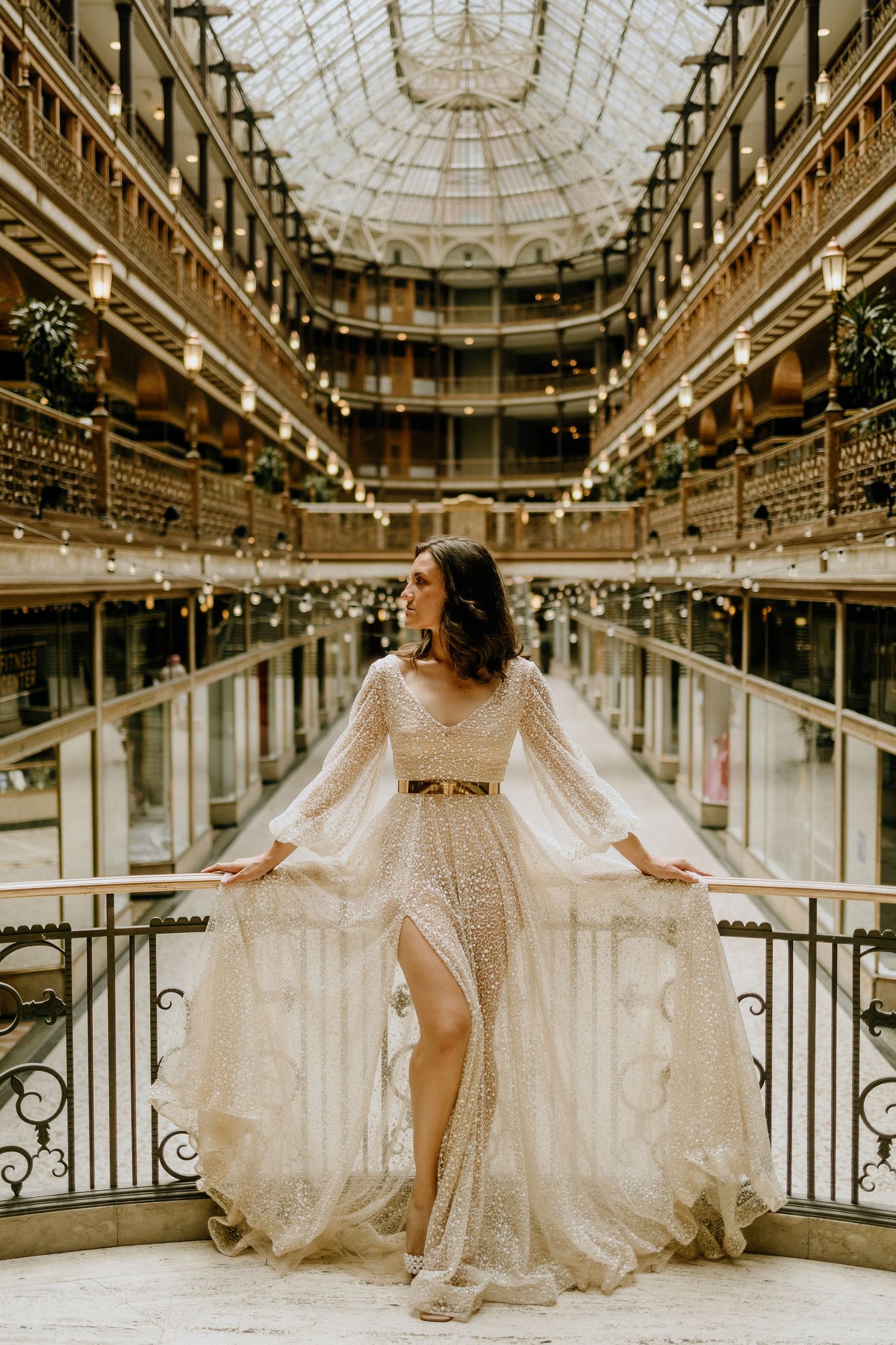 An elegant lace gown shimmers beneath a glass dome in a historic arcade.
