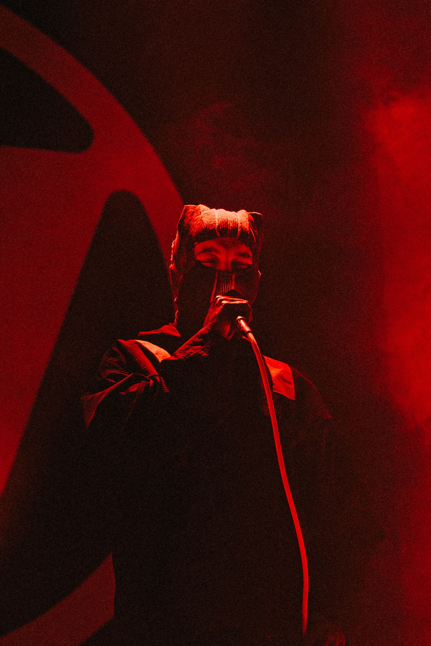 Concert performer silhouetted in dramatic red lighting on stage with microphone.