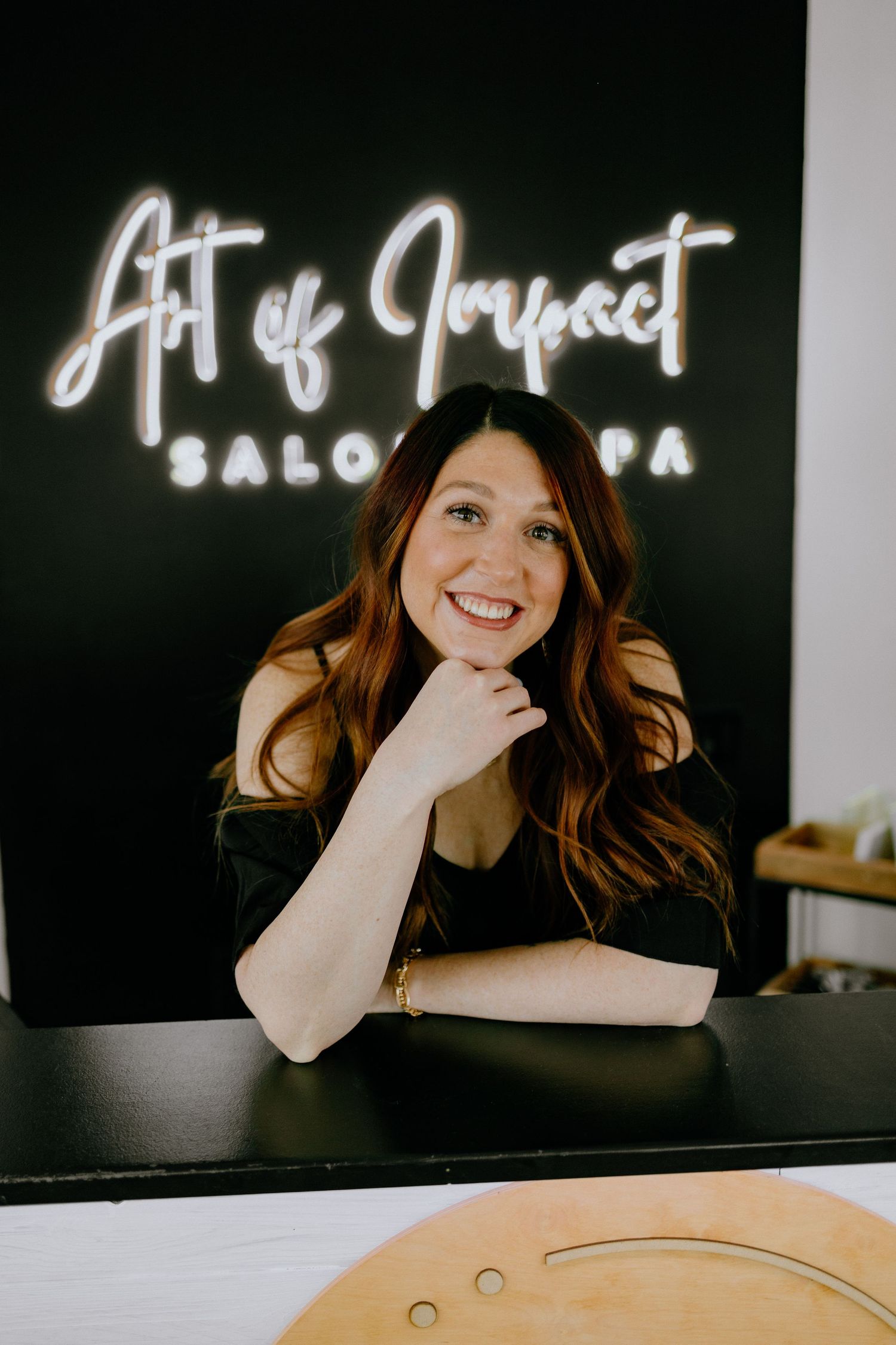 Person poses at salon counter with illuminated 'Art of Impact' neon sign.