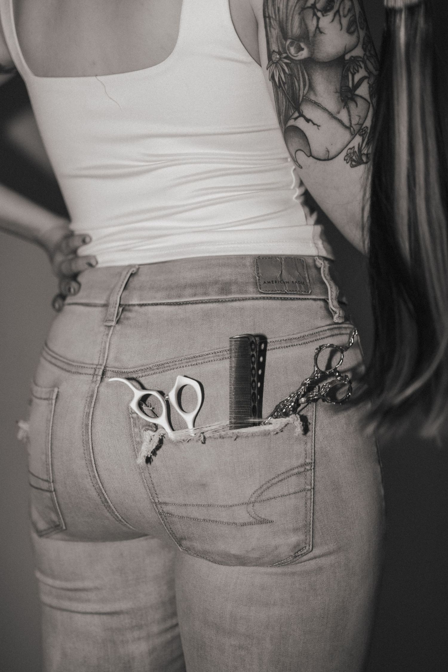 Close-up of scissors in back pocket of jeans with white tank top.