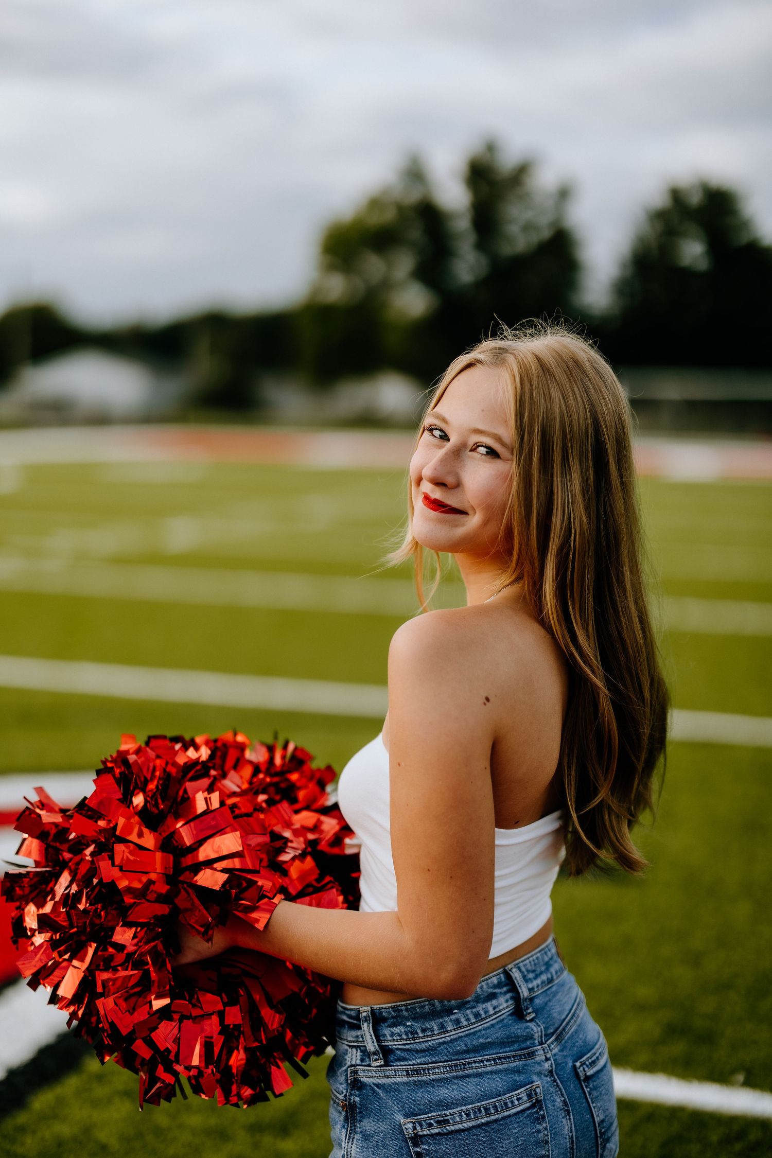 Portrait on football field with red pom poms and casual attire.