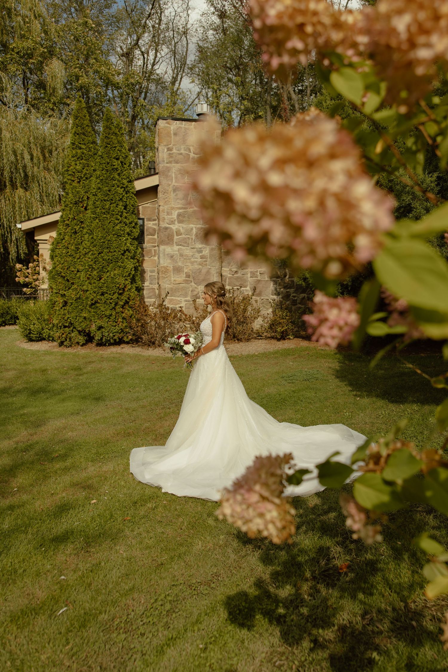 A bride in a flowing white gown twirls gracefully in a garden setting during golden hour.