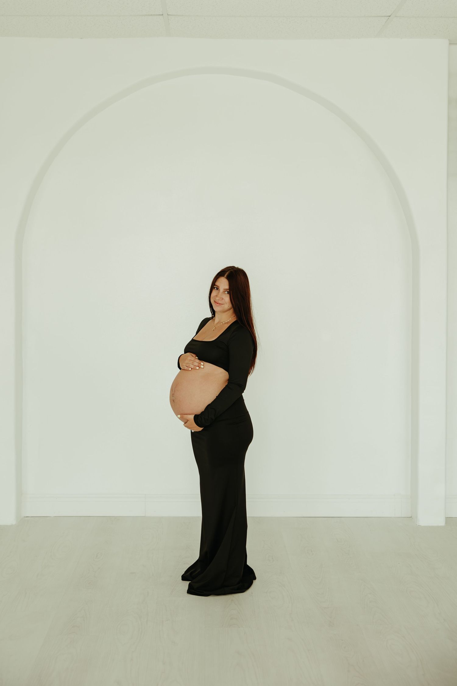 Maternity photo series showing pregnancy progression against white walls in a minimalist style.