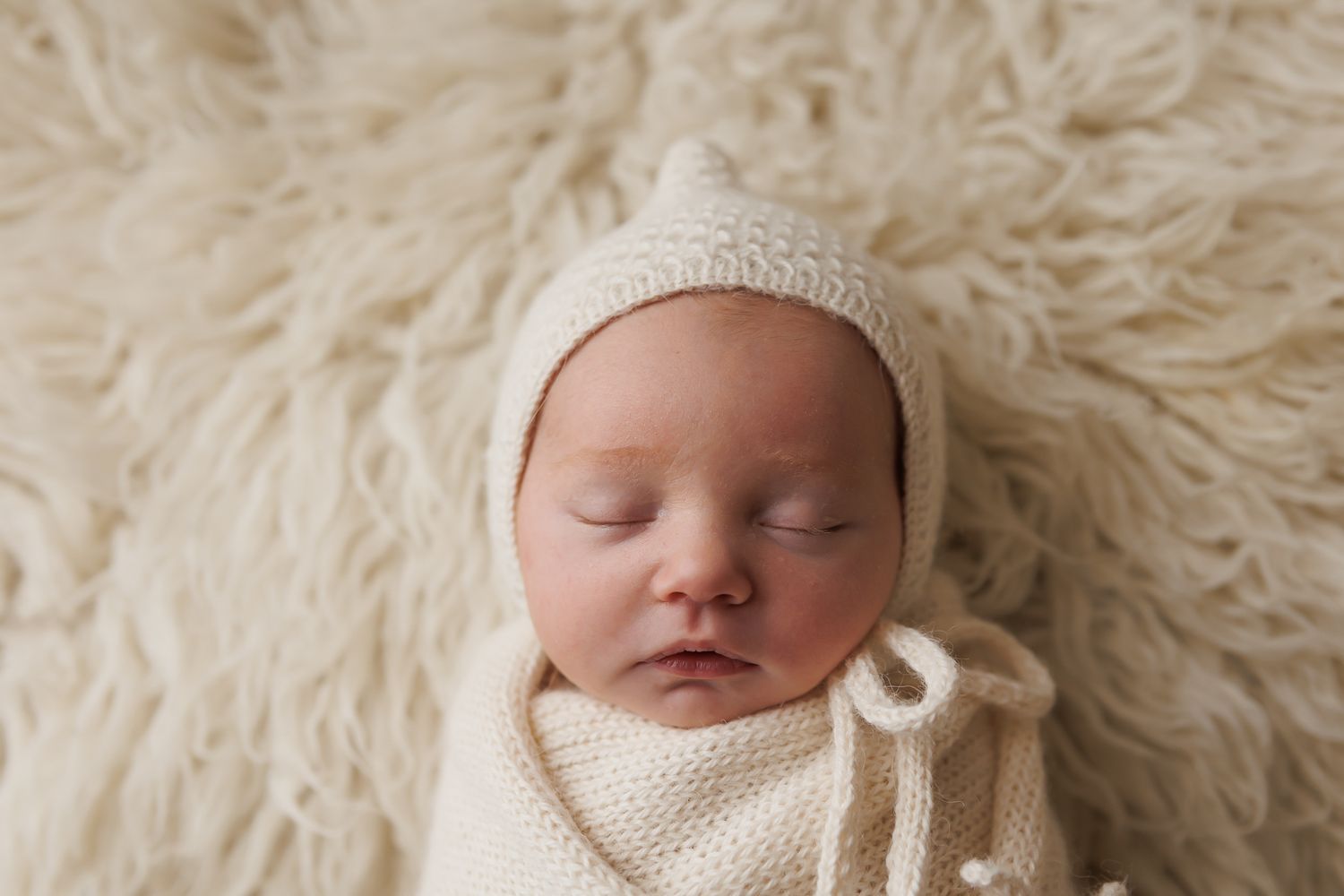 Newborn tightly swaddled in a soft wrap, lying on a matching textured background.