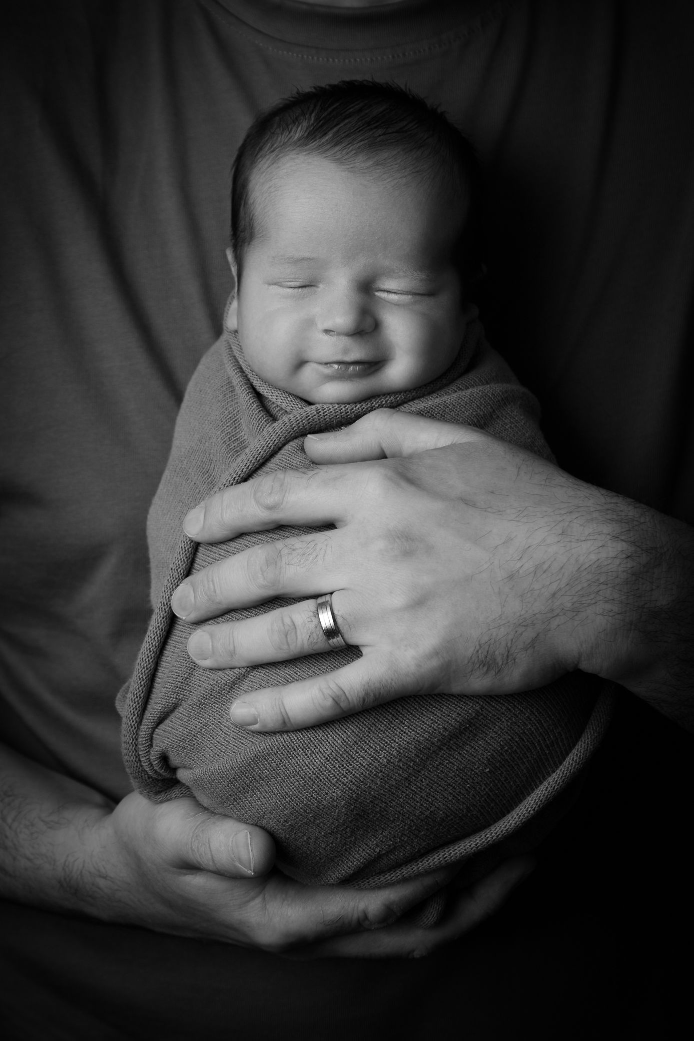 Close-up of a person holding a baby, wearing a ring, in a black and white photo.