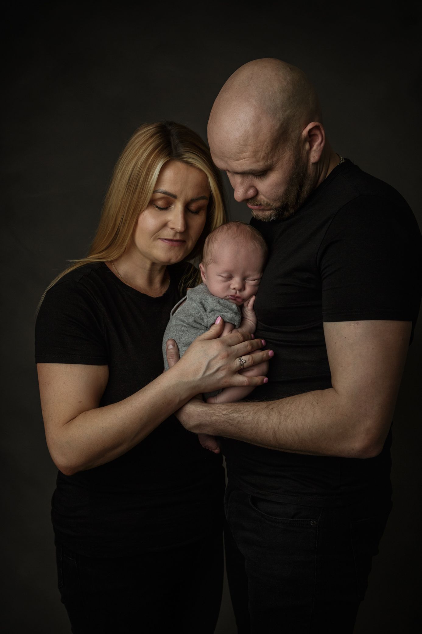 A couple joyfully holds their newborn son, creating a heartwarming scene set against a deep black background.