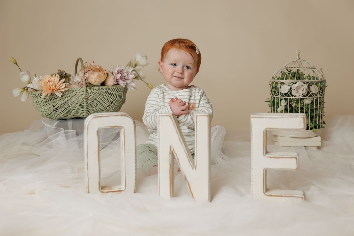 one year old girl sitting on a soft rug with the letters O N E in front of her