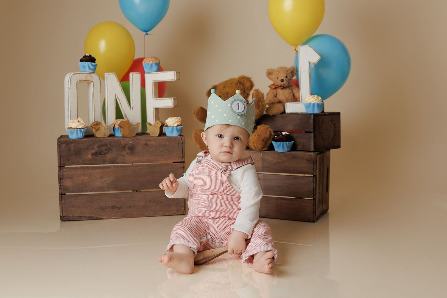 one year old baby boy sitting on a cream background with balloons and other birthday decorations