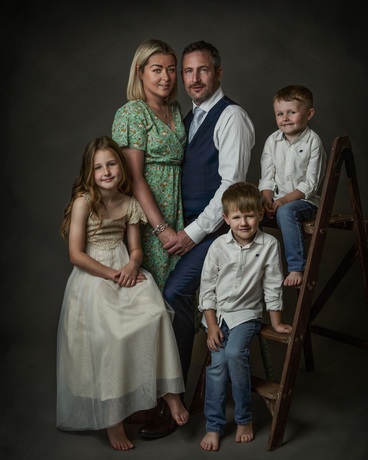 a family of parents and three children sitting and standing in various poses on a dark background
