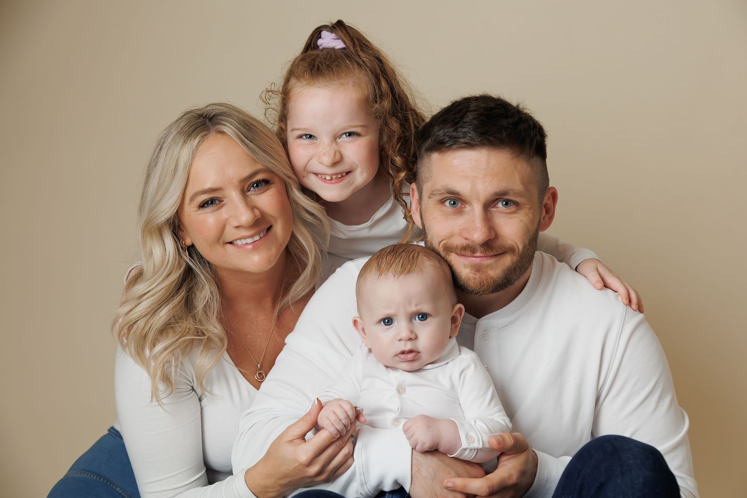 a young family of four on a beige backdrop all smiling at the camera