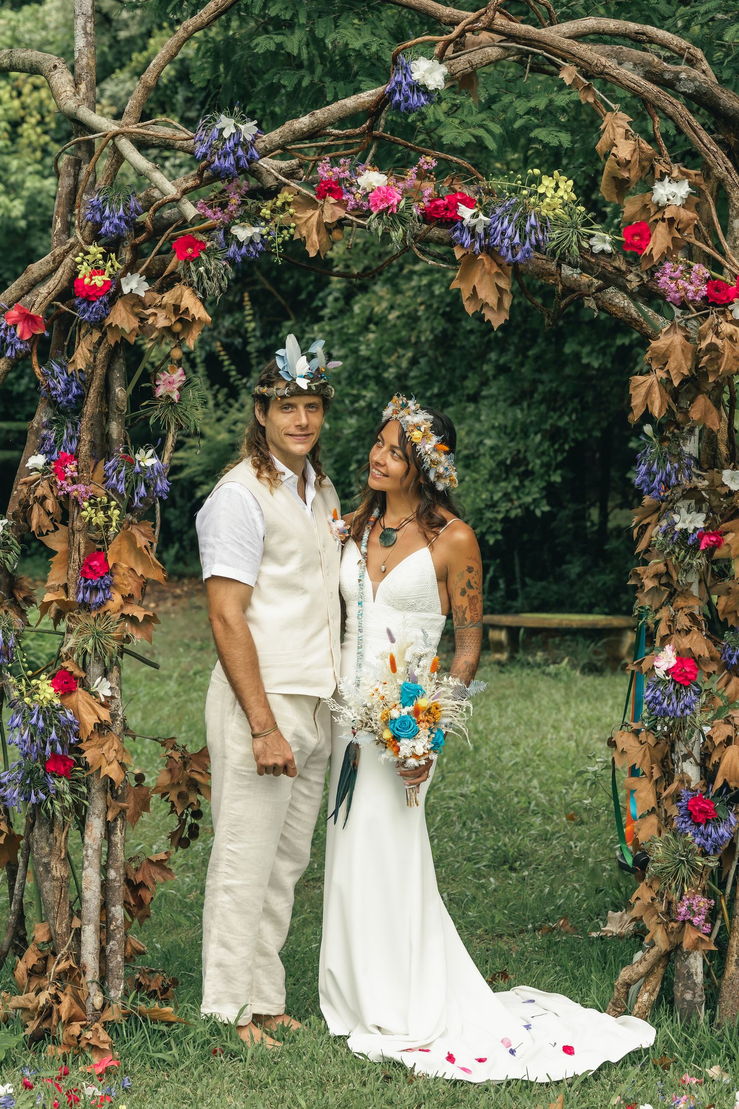 a couple stand under an archway of flowers at their wedding