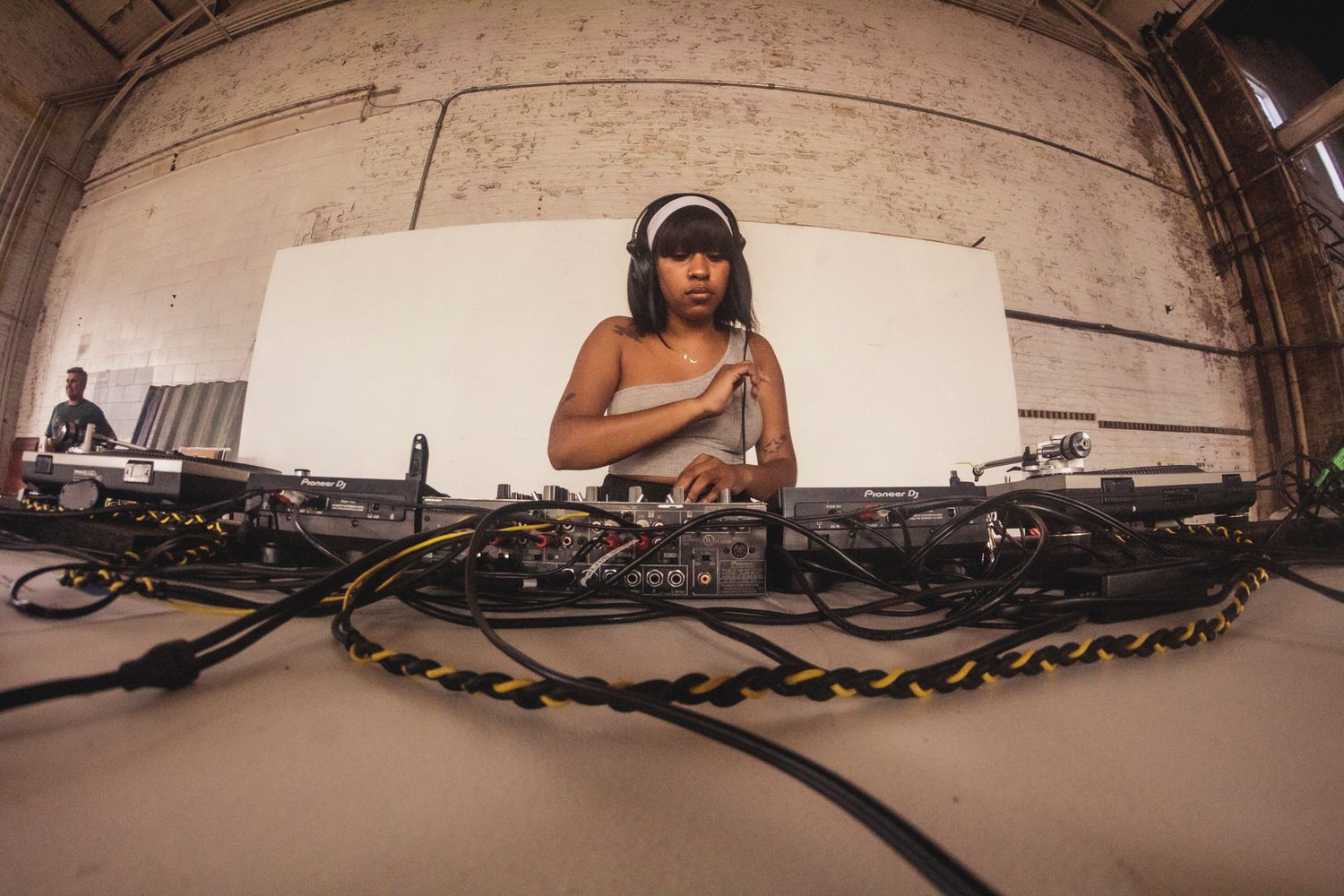 A DJ performs at their equipment setup under an industrial arch.