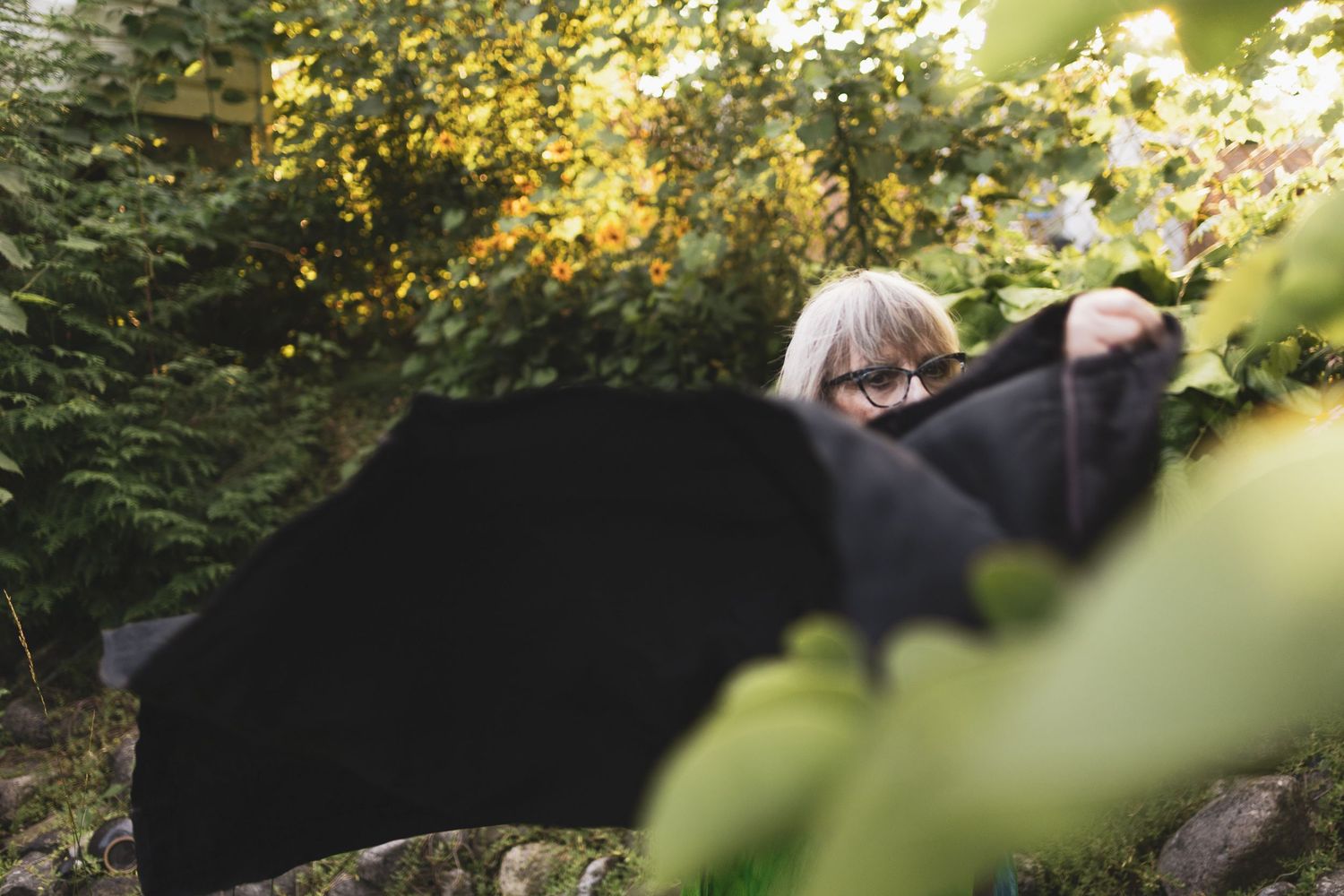 A dreamy outdoor portrait of an older woman in a garden with black fabric flowing in the golden sunlight.