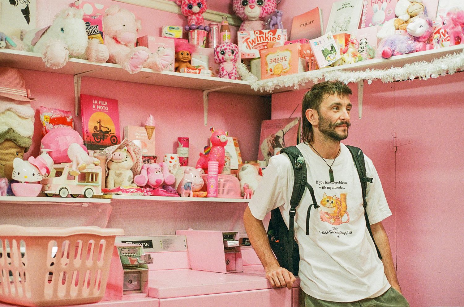 Pink kawaii merchandise and toys fill the shelves of a vibrant retail display and a male figure posing.