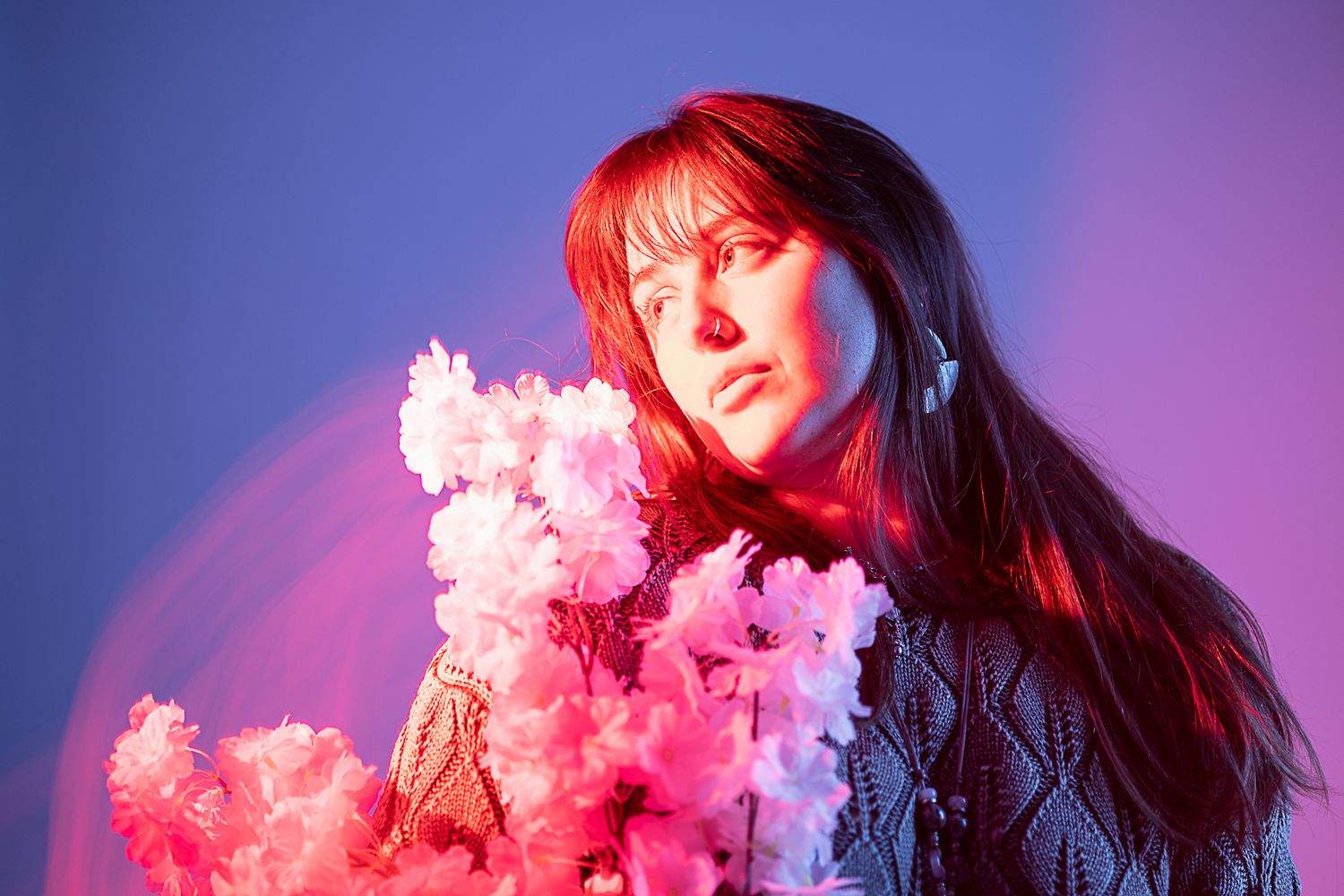 Ethereal portrait with pink lighting and cherry blossoms creating dreamy atmosphere.