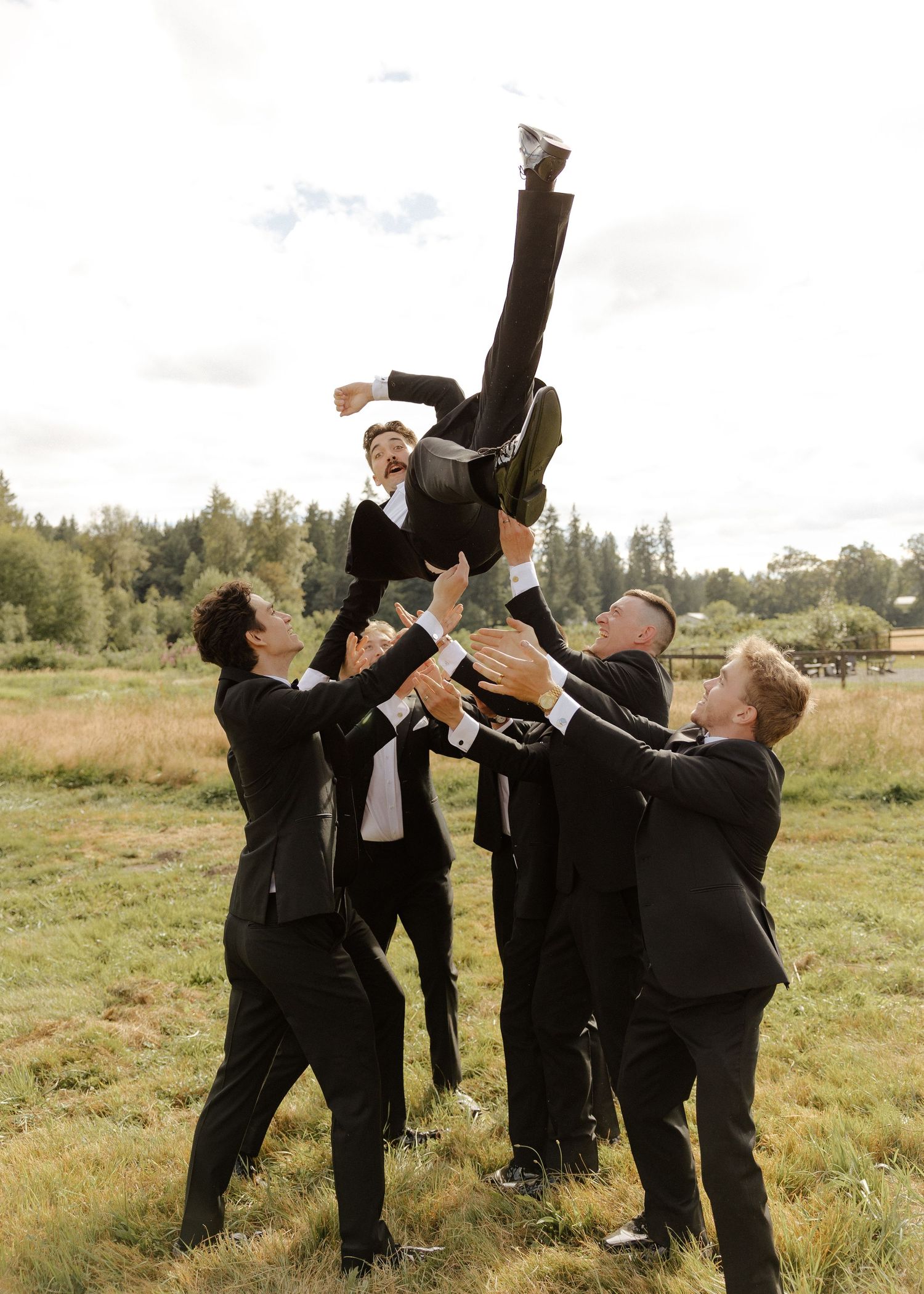 Groomsmen toss the groom into the air in a celebratory outdoor wedding party photo.