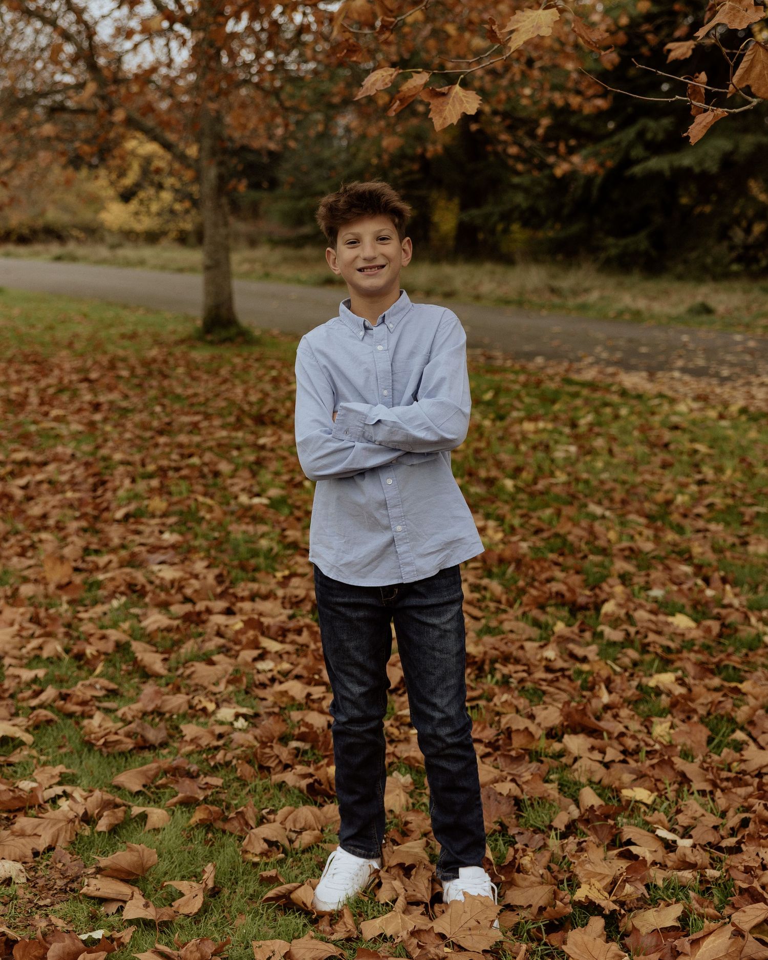 A young person poses with crossed arms among fallen autumn leaves.