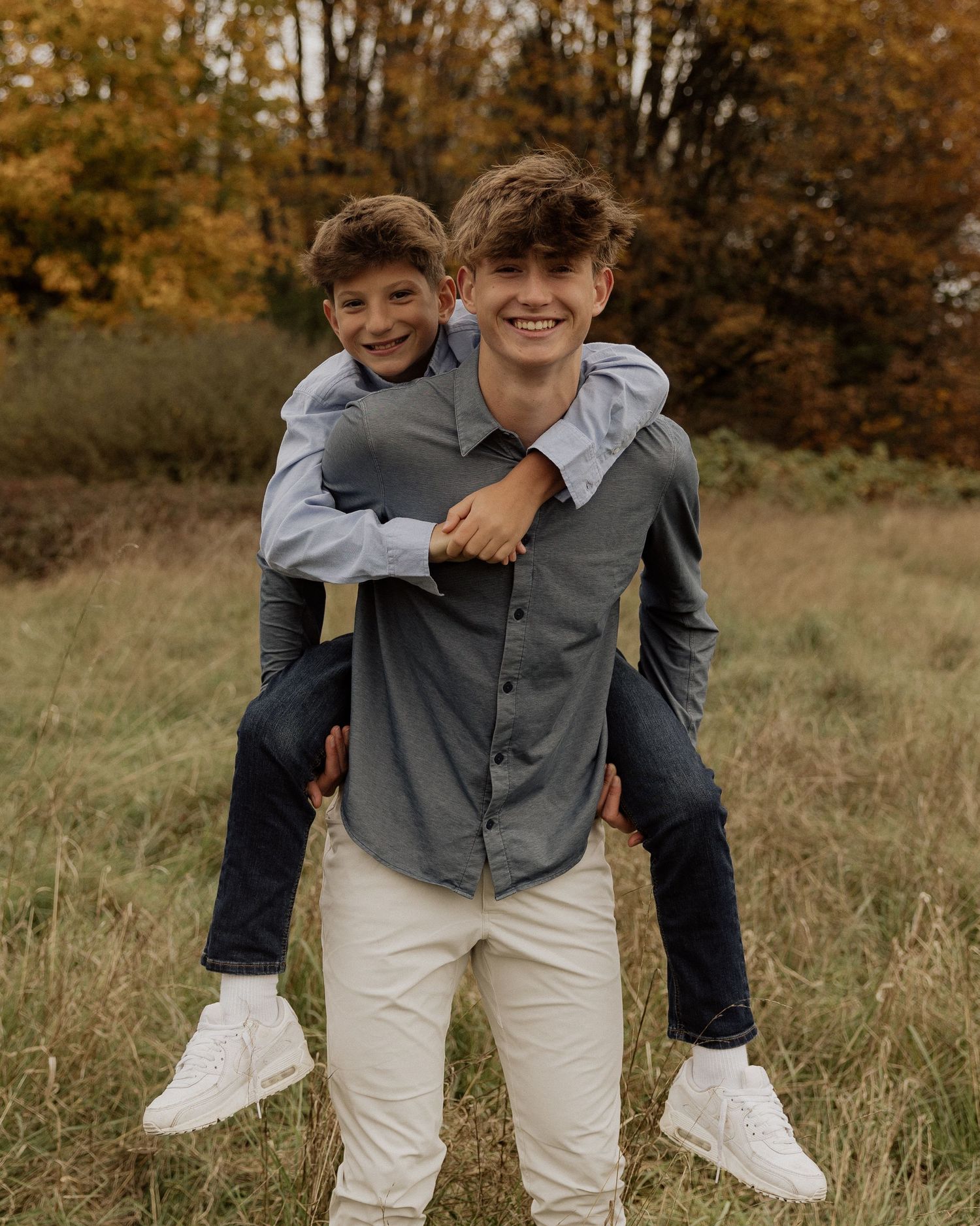 Playful piggyback pose in an autumn field with golden trees in background.