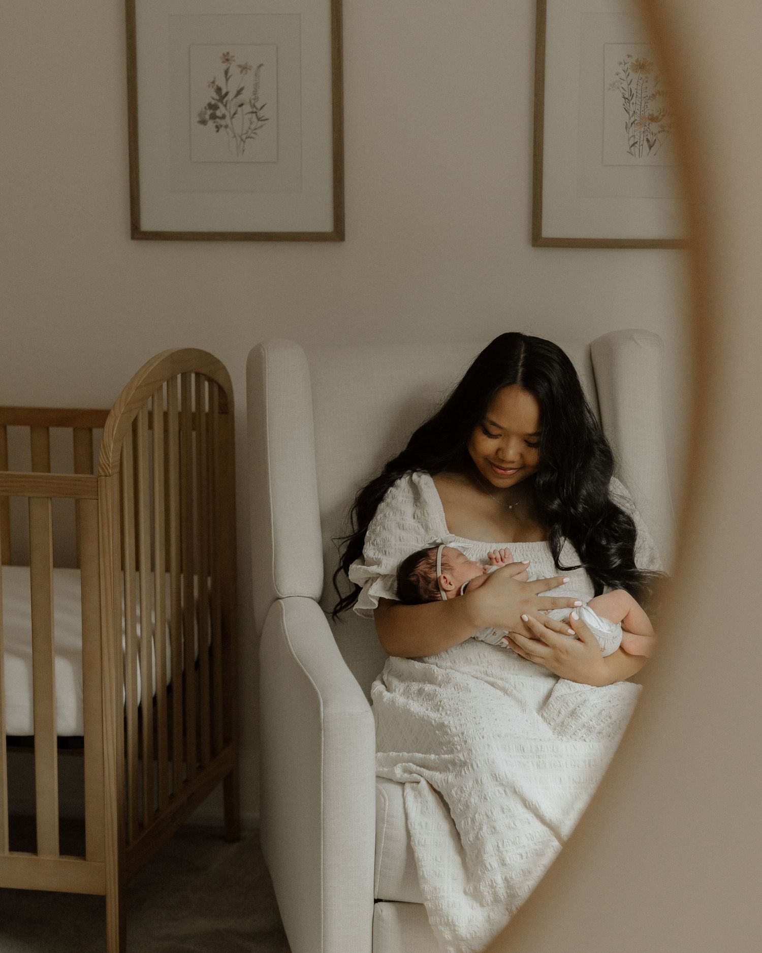 Intimate nursery scene with mother and baby sharing quiet moment in white armchair.