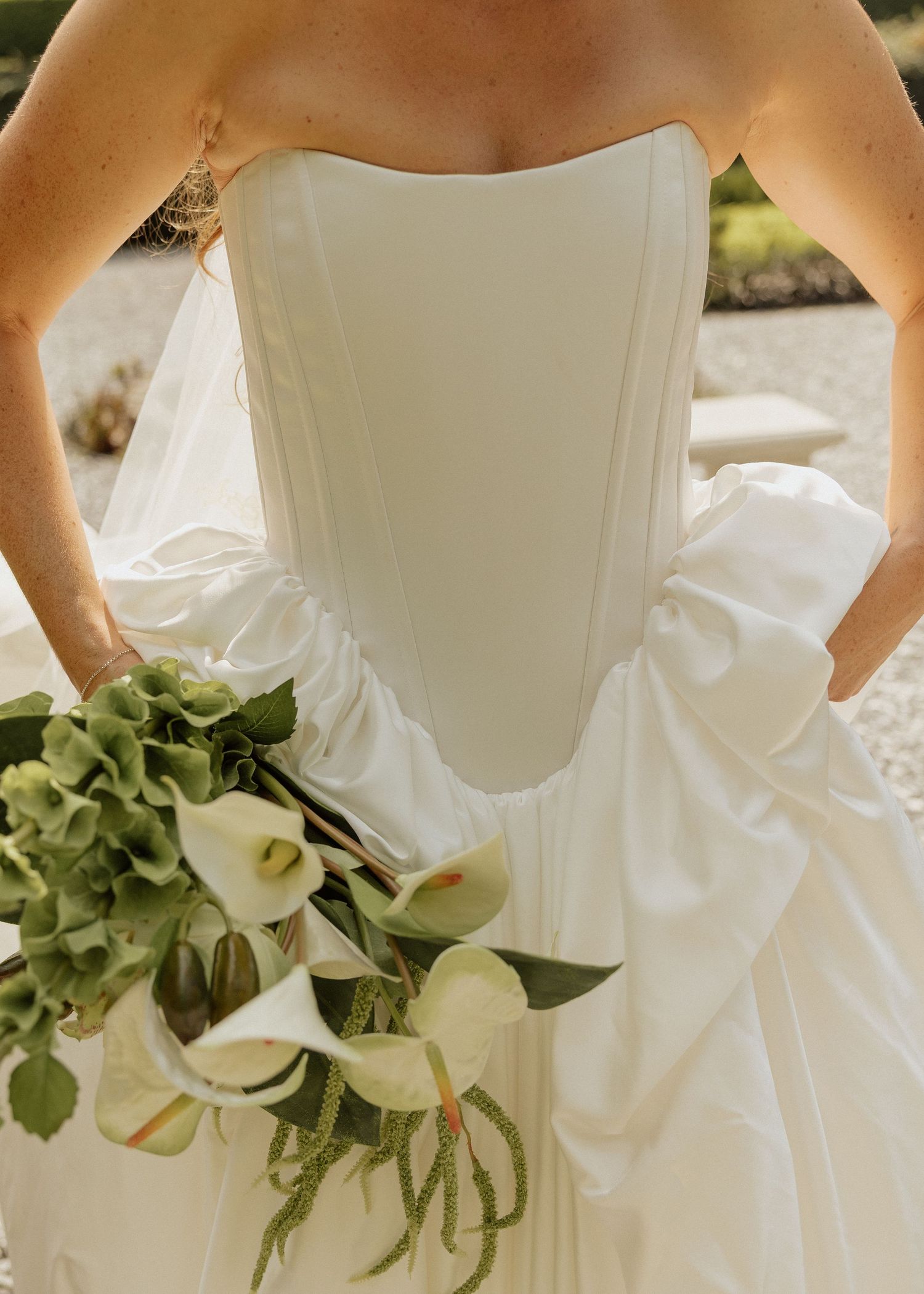 Bride in strapless white corset wedding gown holding elegant bouquet of white calla lilies and green hydrangeas.
