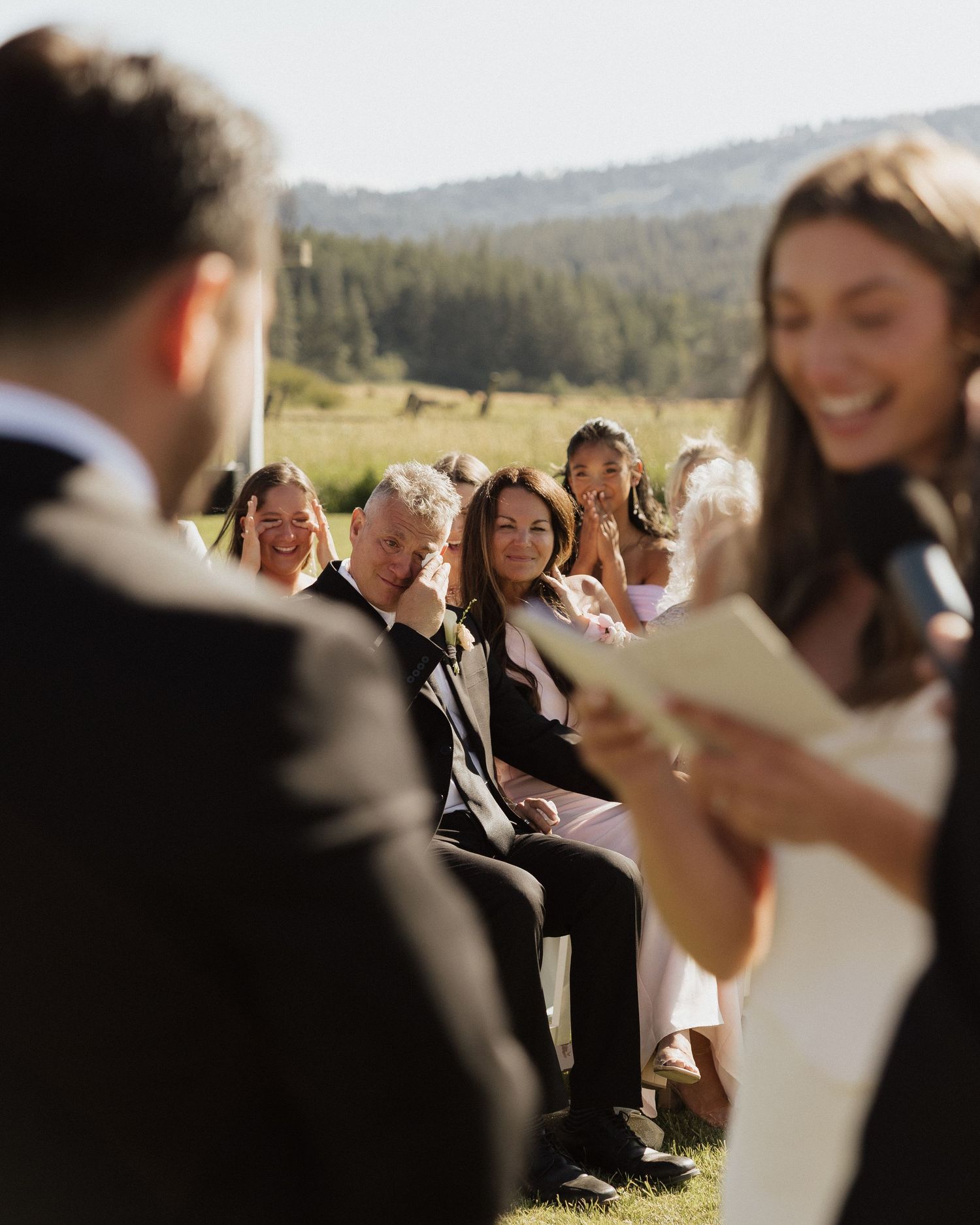Wedding guests smile and cry with emotion during outdoor ceremony vows with mountain backdrop.