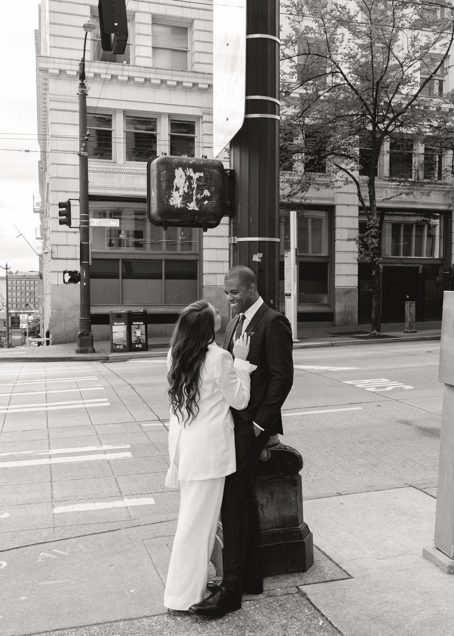Black and white photo of a couple in wedding attire sharing an intimate moment on a city street corner.