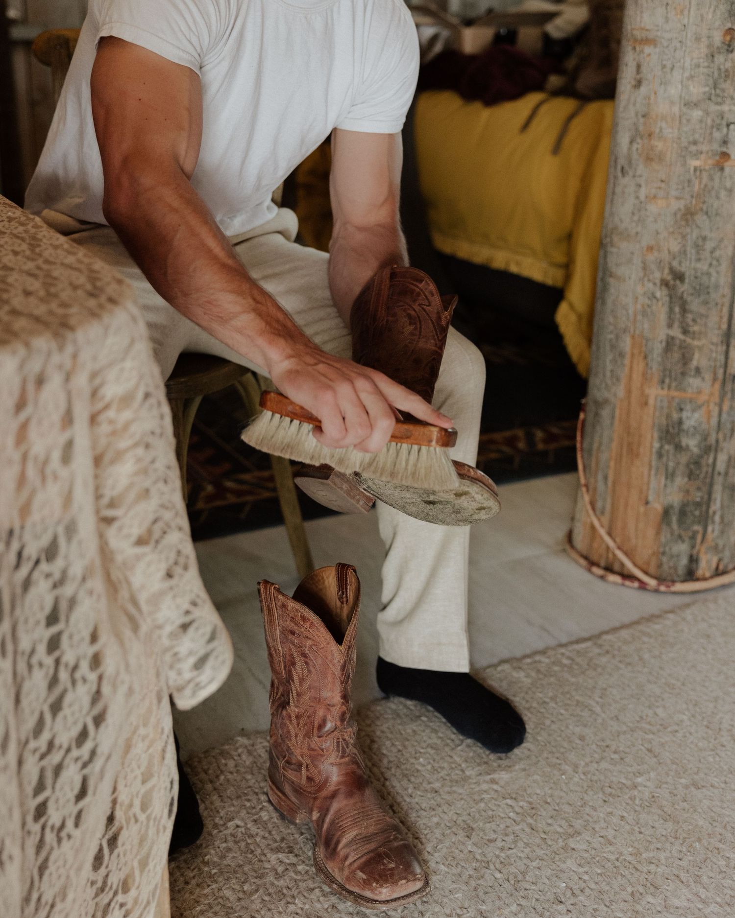Someone brushing brown leather cowboy boots on carpet while wearing a white shirt.