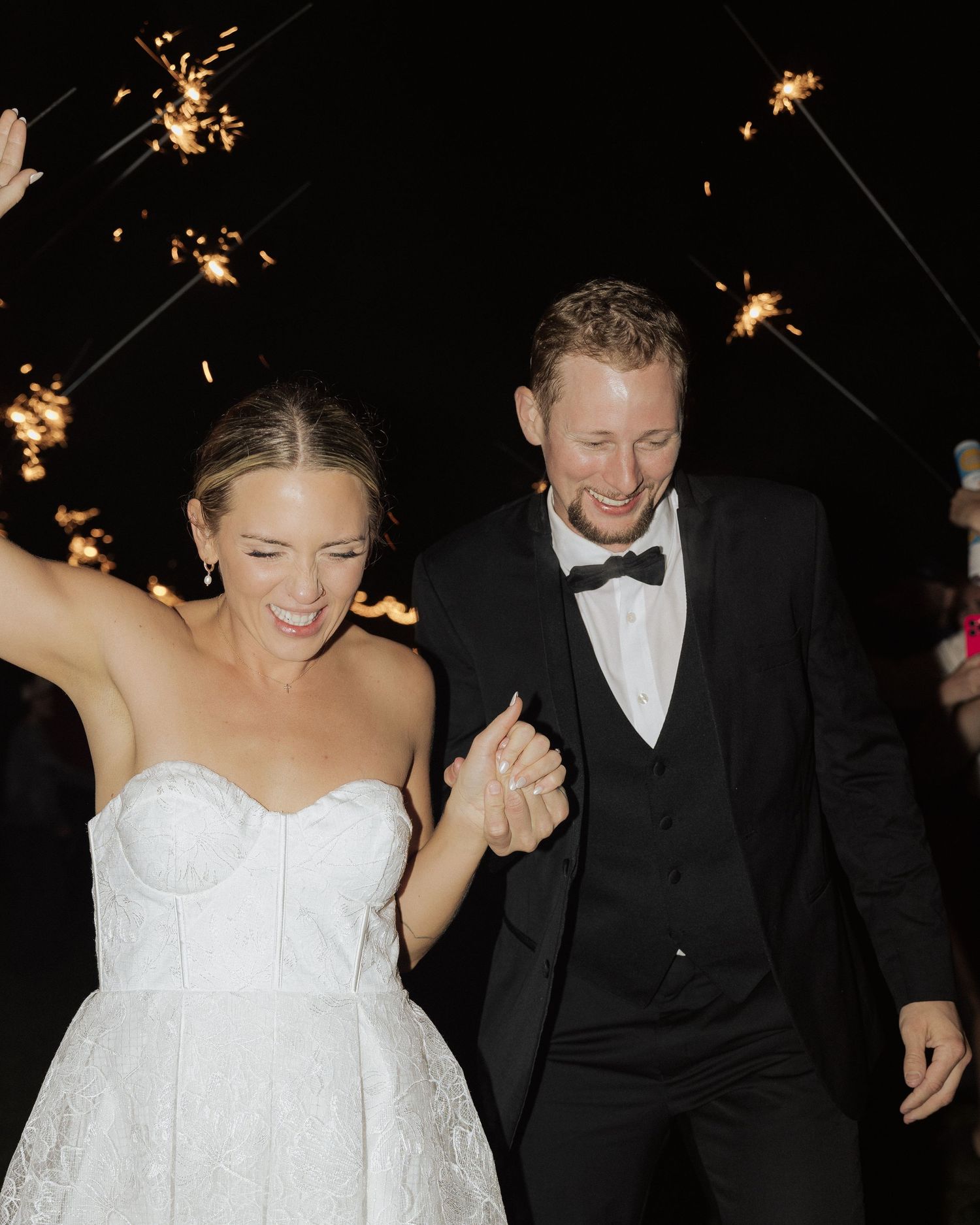 Newlyweds share joyful moment under sparklers at outdoor evening wedding celebration.