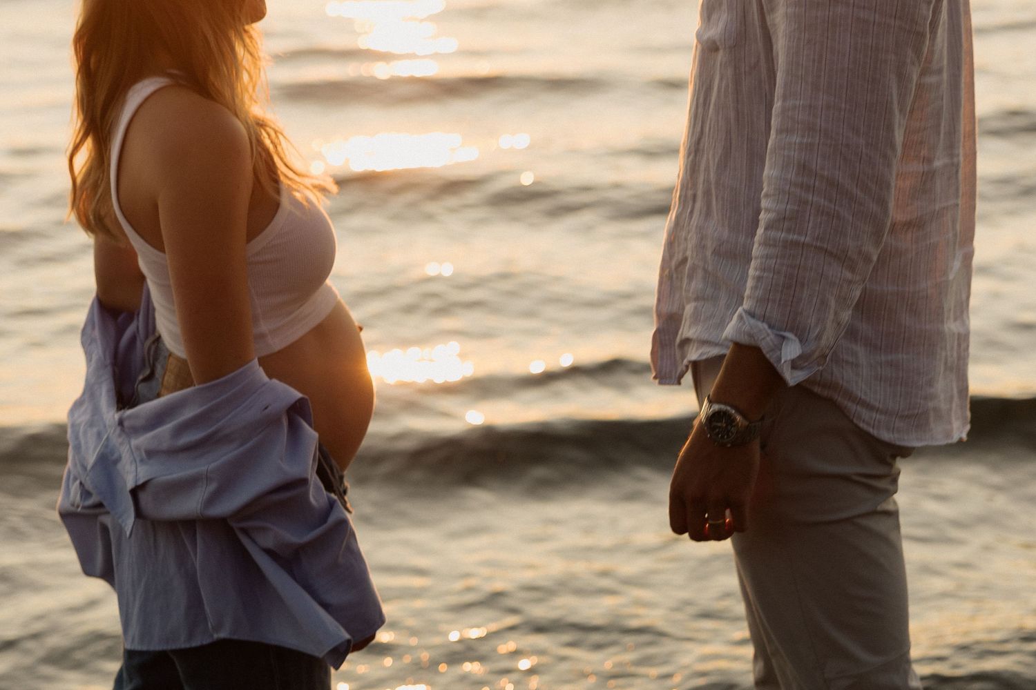 Side view of expecting couple at sunset on beach.