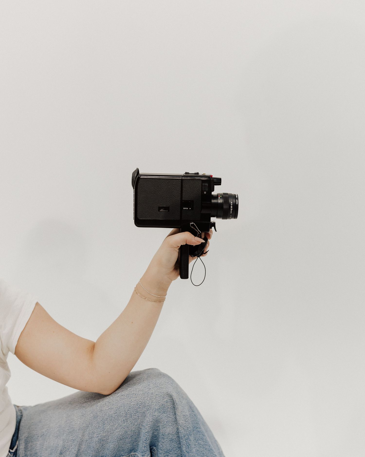 Hand holding a vintage camera against white background in minimal composition.