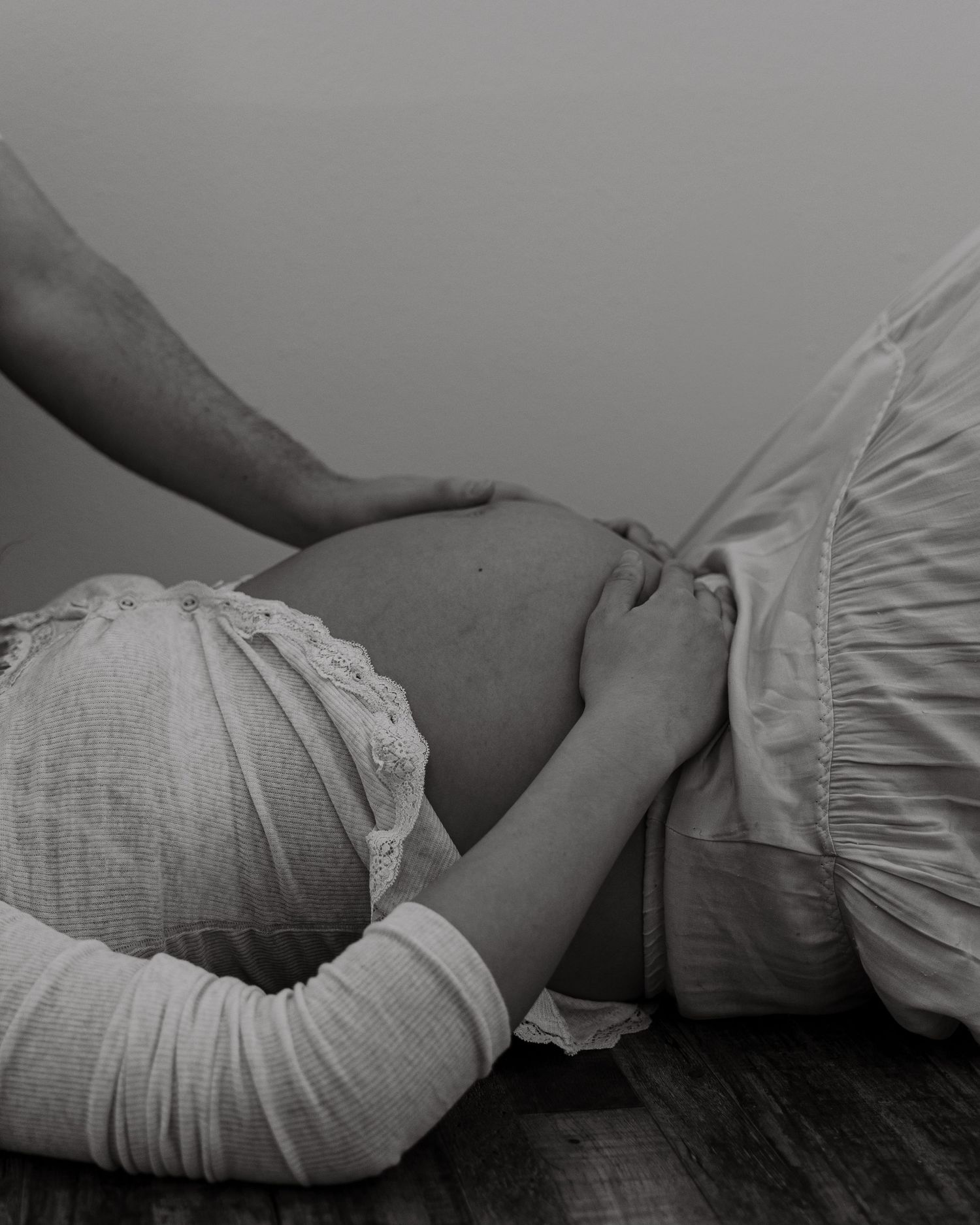 Black and white image of hands cradling a pregnant belly on wooden floor.