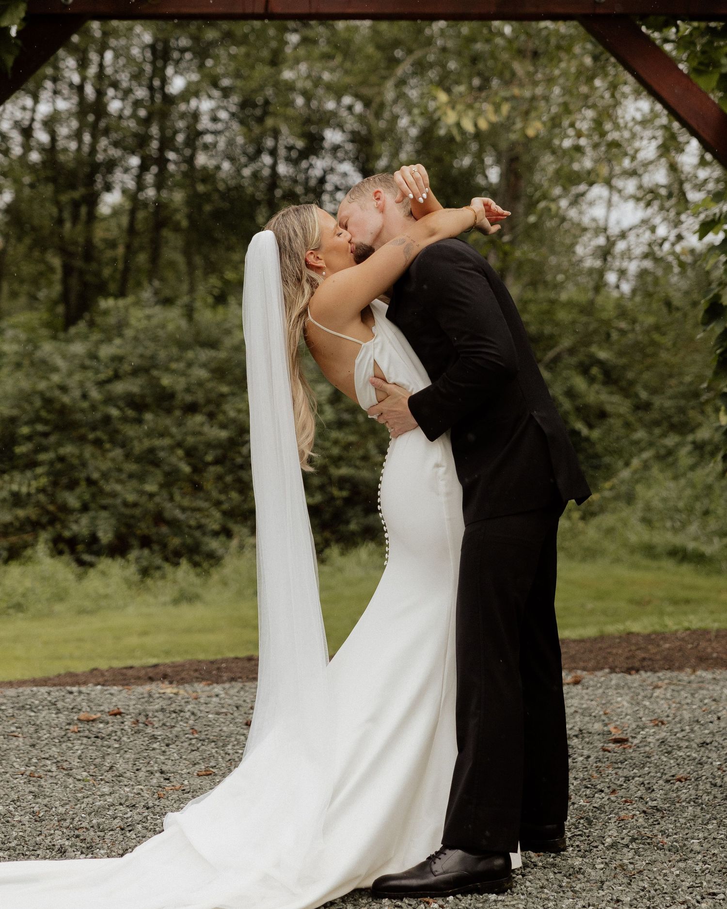 A passionate dip kiss during wedding ceremony under wooden pergola.