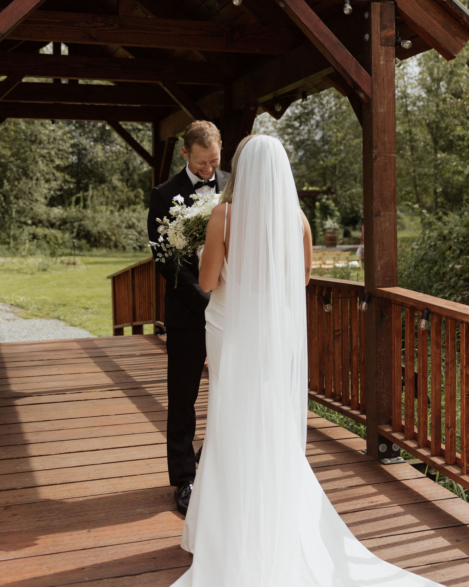 Wedding couple sharing a moment on rustic wooden deck with bride holding white bouquet.
