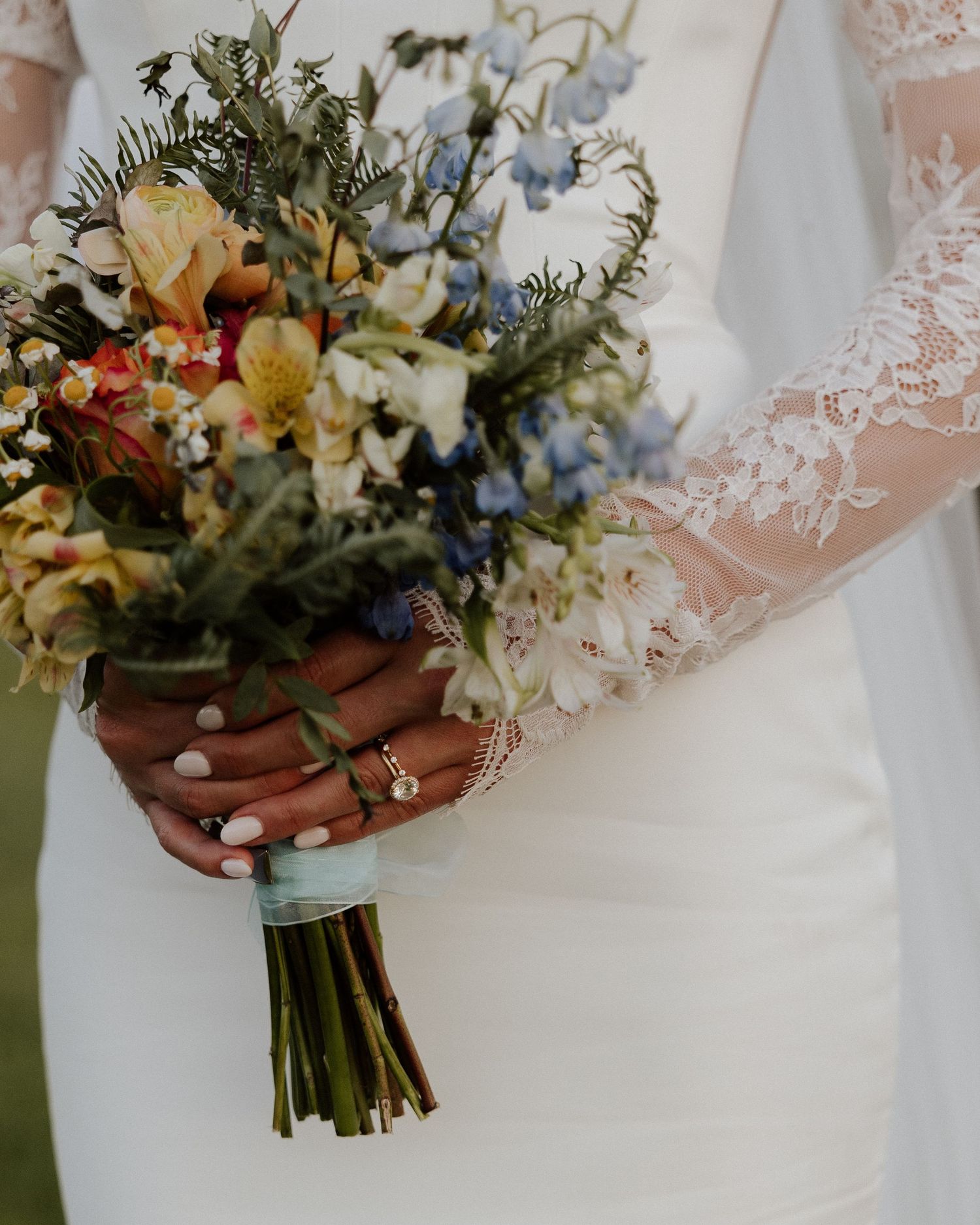 Close-up of wedding bouquet with colorful wildflowers and delicate lace sleeve details.