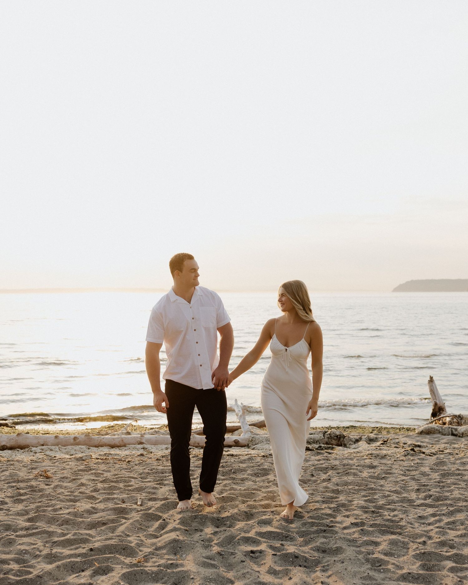 Couple walking on beach at sunset in casual attire.
