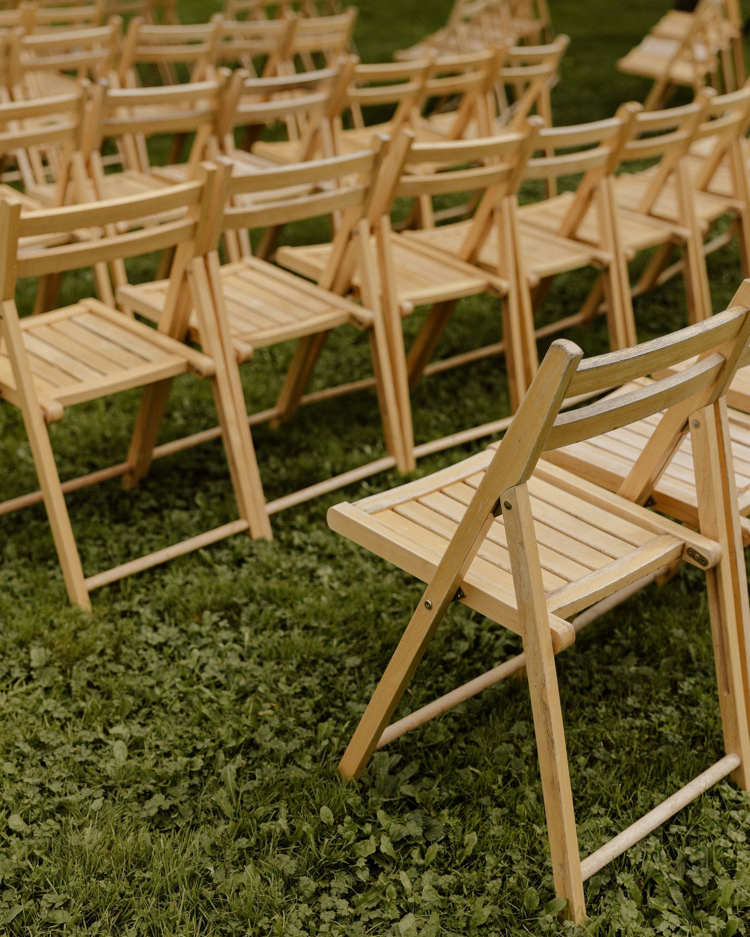 Rows of wooden folding chairs arranged on grass for an outdoor event.