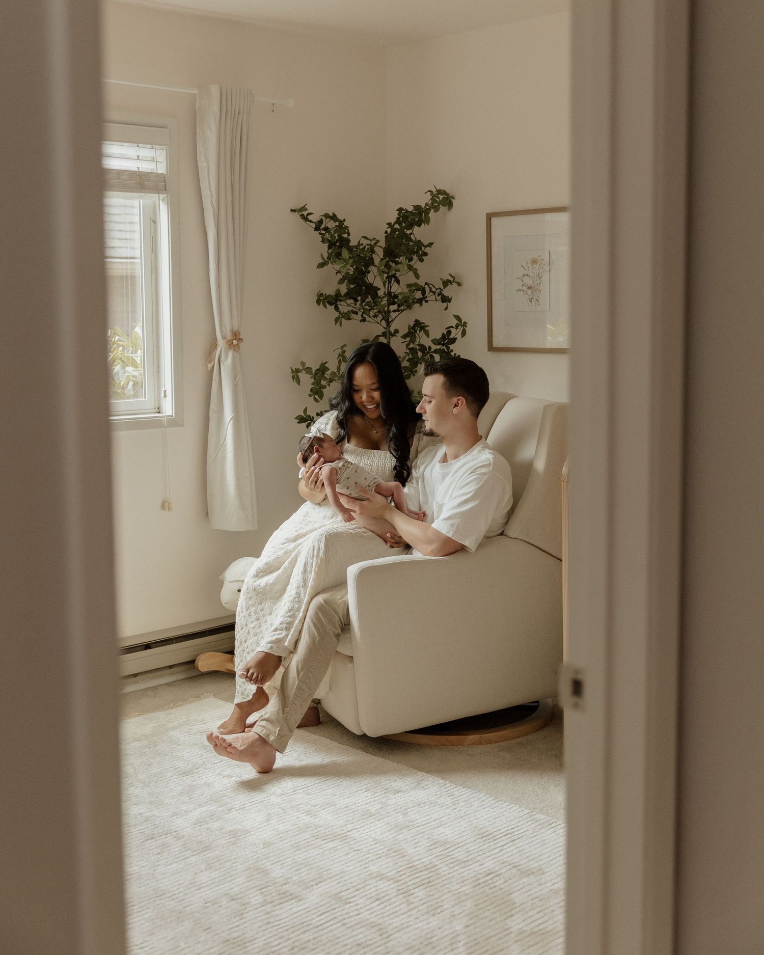 Family relaxing together with newborn in cozy nursery, viewed through doorway.