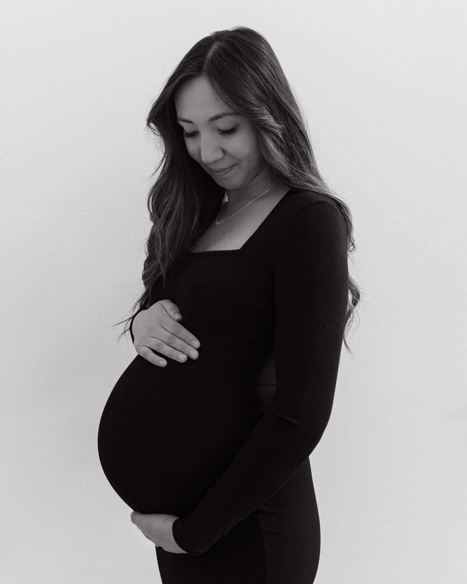 An elegant side profile maternity portrait in black and white against a plain backdrop.