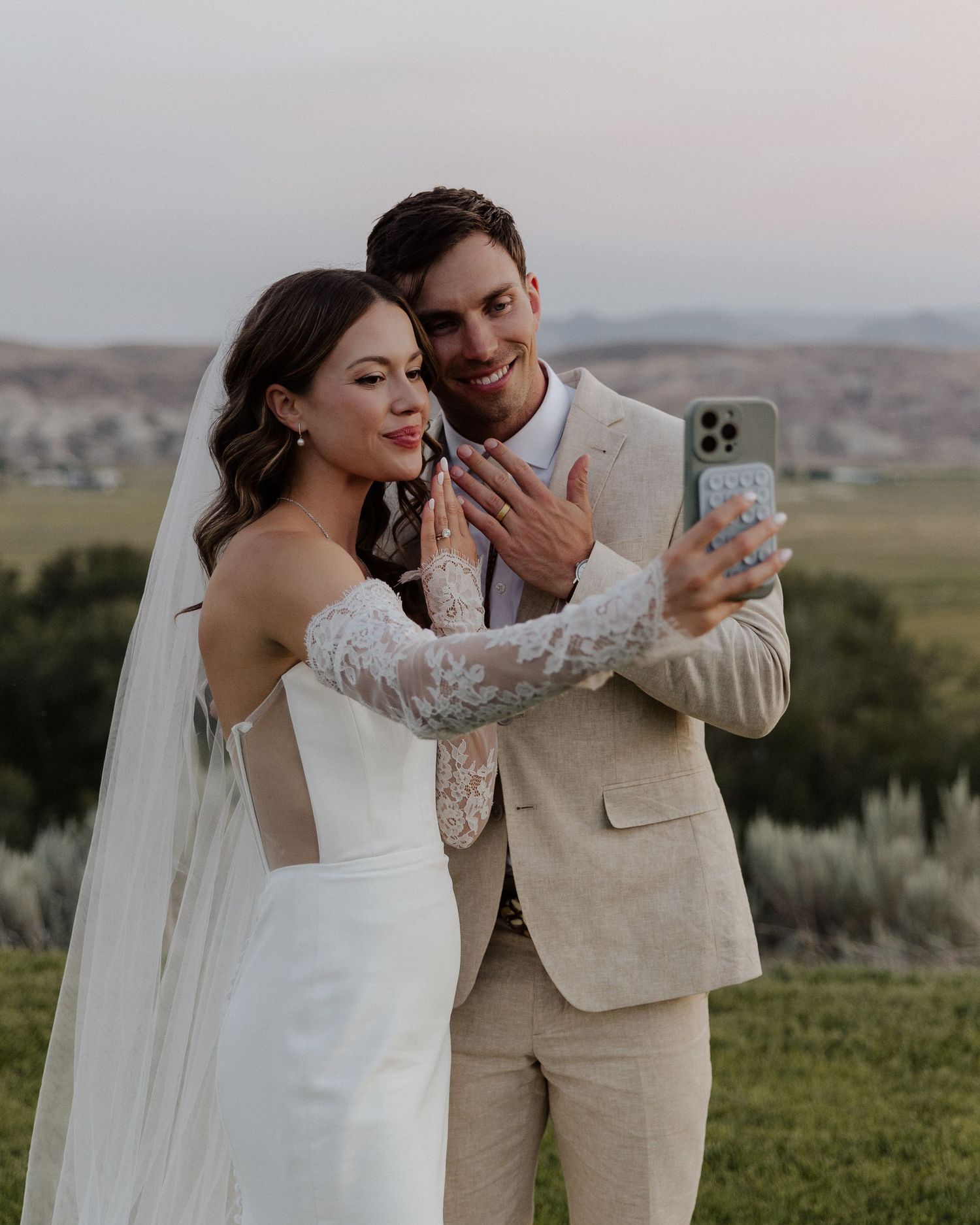 Wedding couple taking selfie together outdoors with mountain landscape behind them.