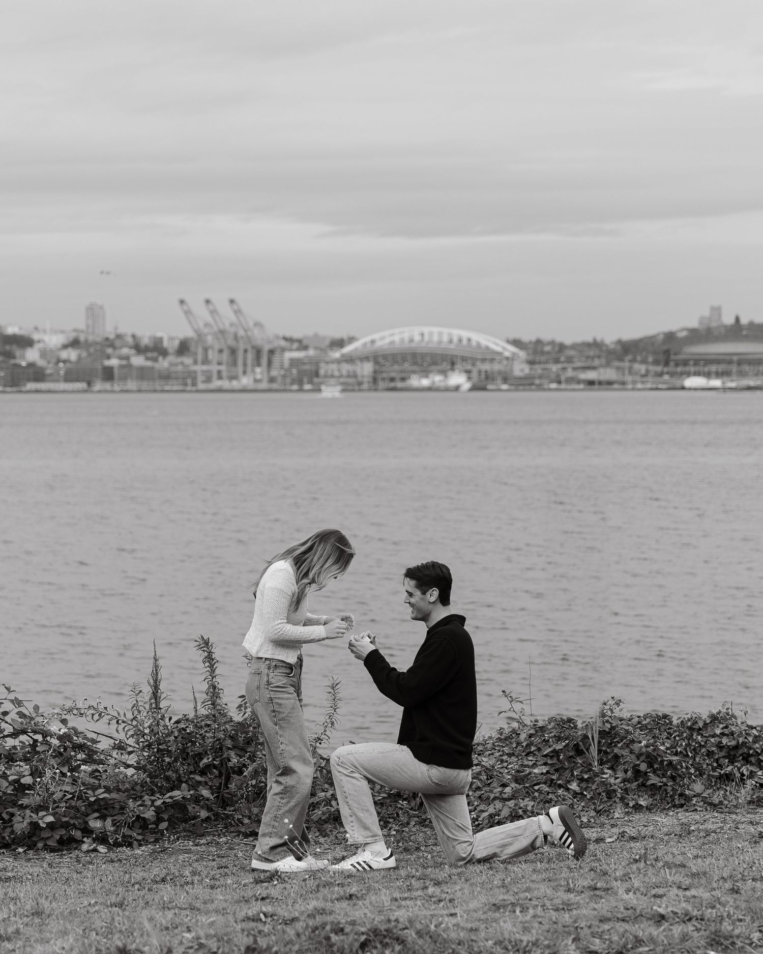 Romantic proposal scene with harbor bridge and industrial port in background.