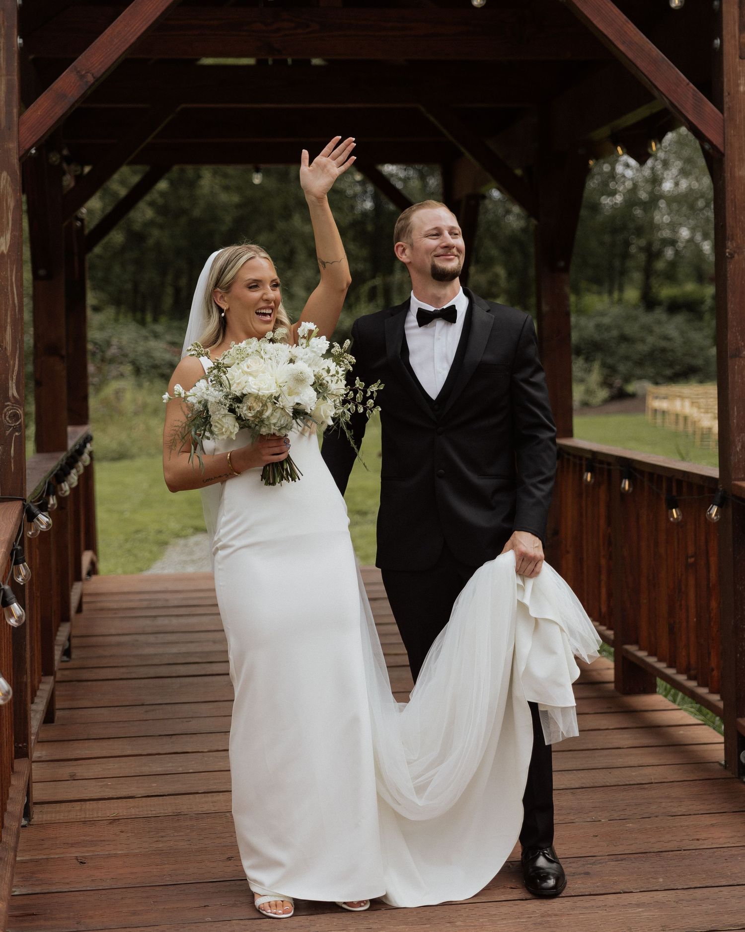 Joyful newlyweds celebrating on wooden bridge deck with bride holding white bouquet.