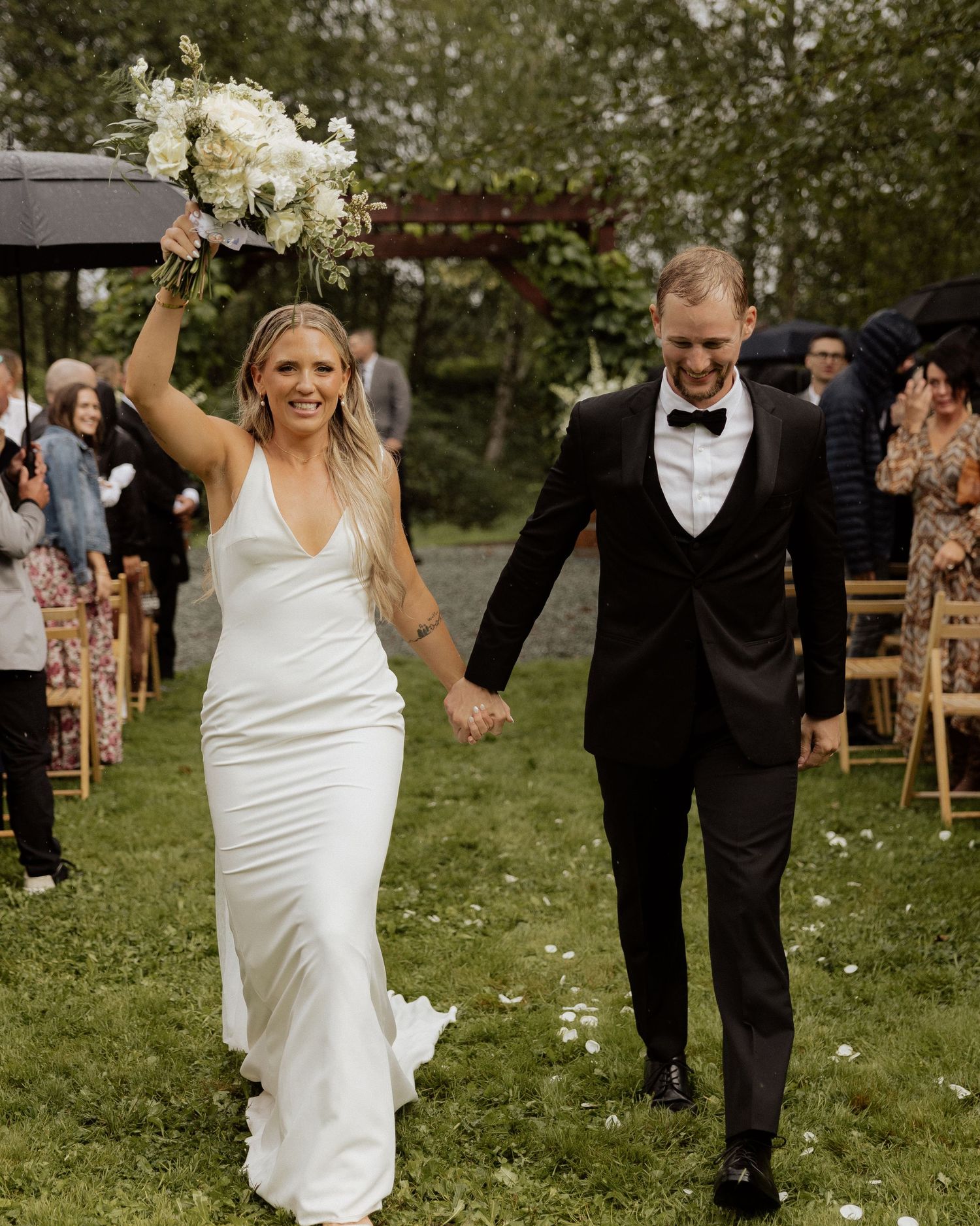 Joyful couple walks down aisle with white floral bouquet raised in celebration.
