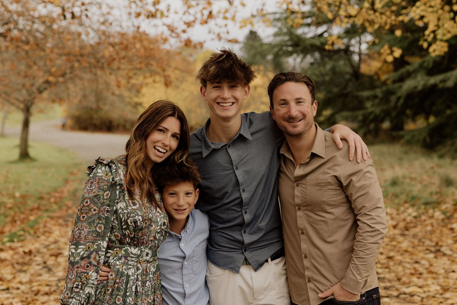 A family of four poses together on an autumn day with golden leaves falling in the background.