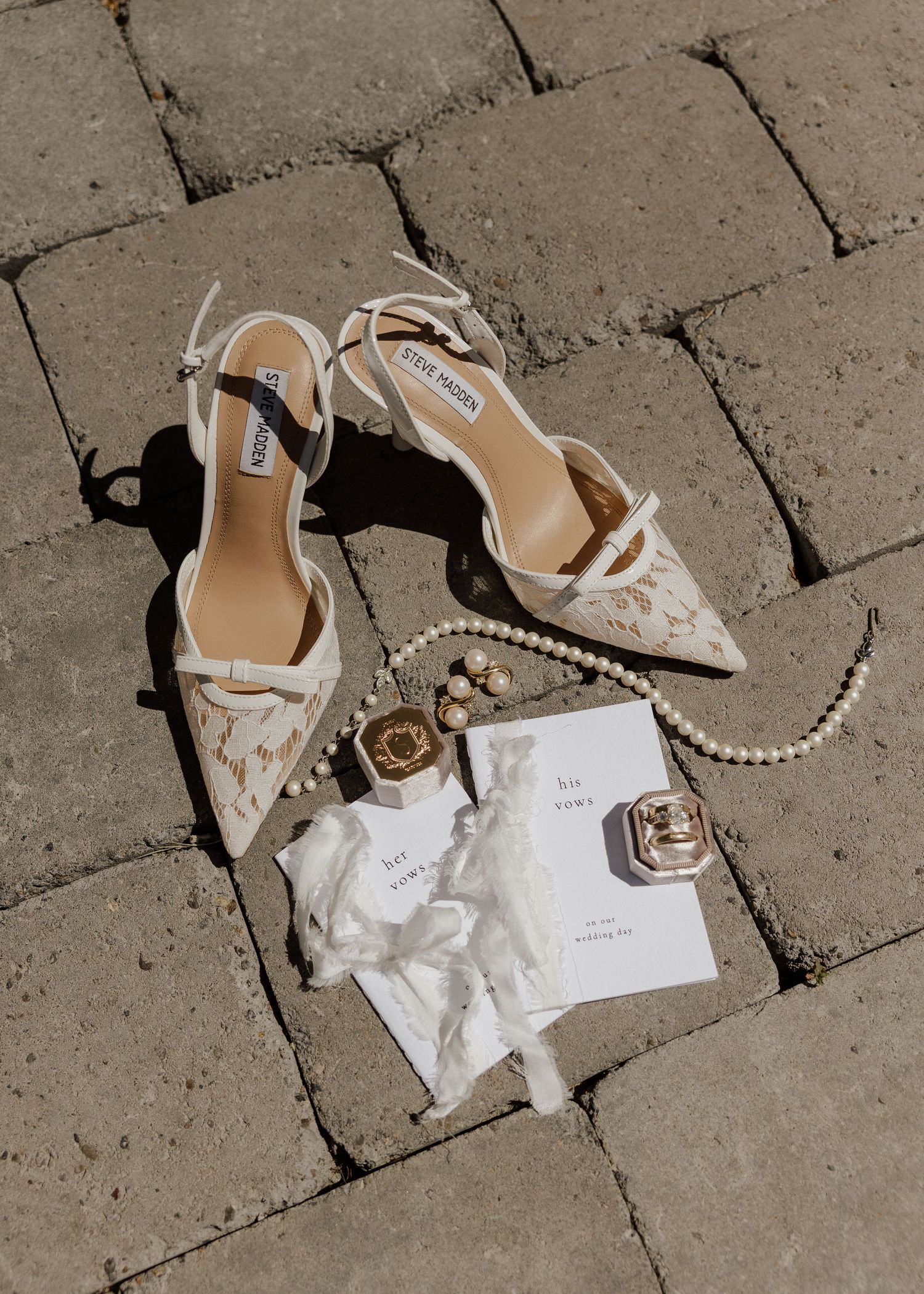 Flat lay of bridal accessories including Steve Madden lace heels, pearl necklace, and vow cards.
