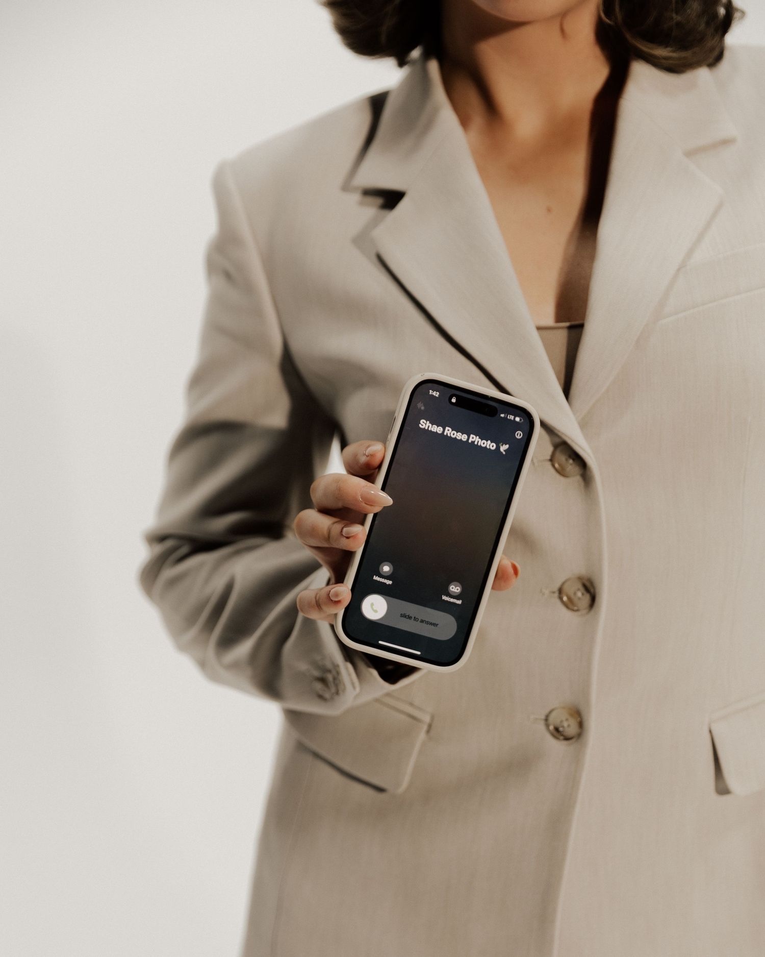 Close-up of person in beige blazer holding smartphone displaying dark screen interface.