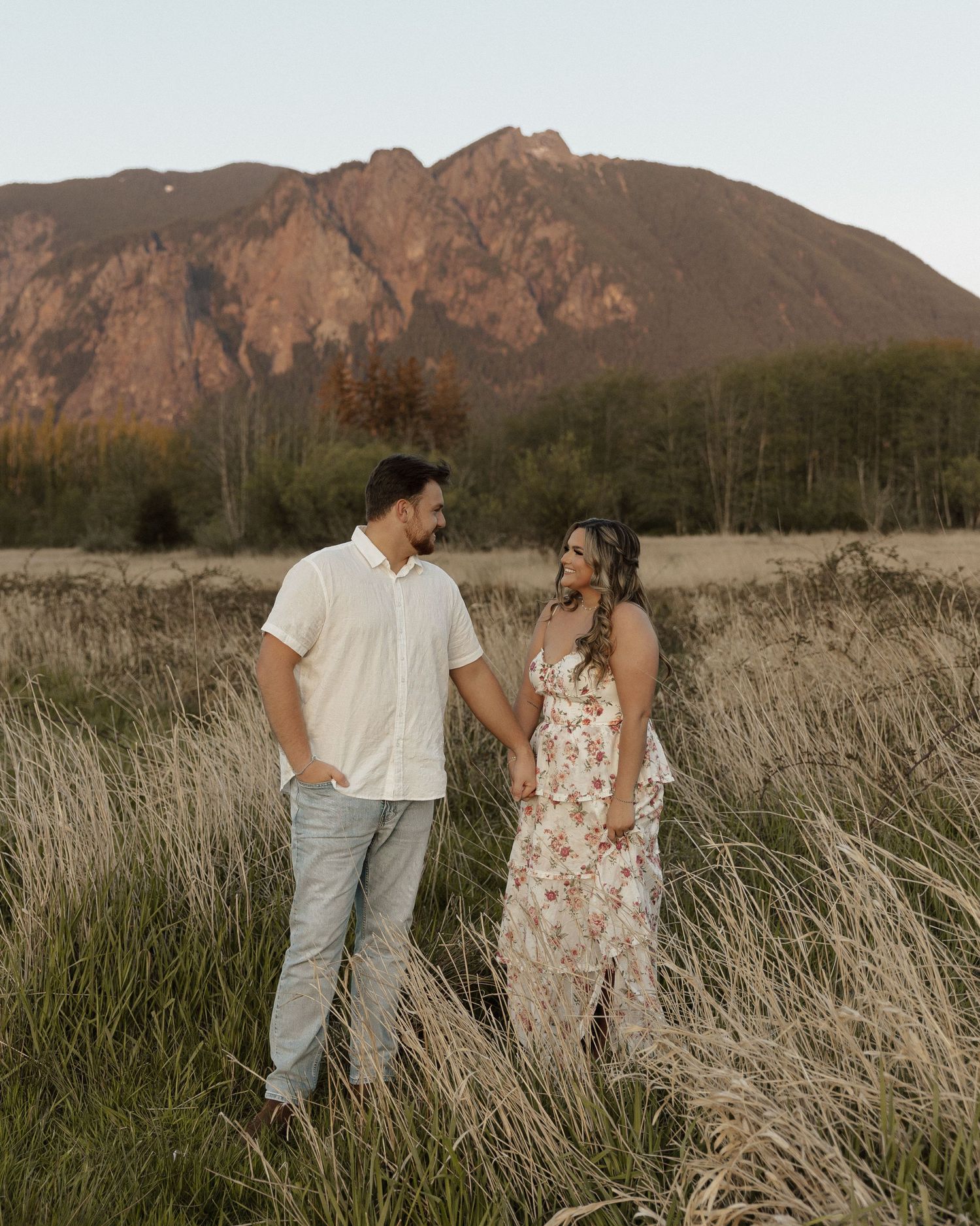 Couple sharing a moment in field with rustic mountain scenery.