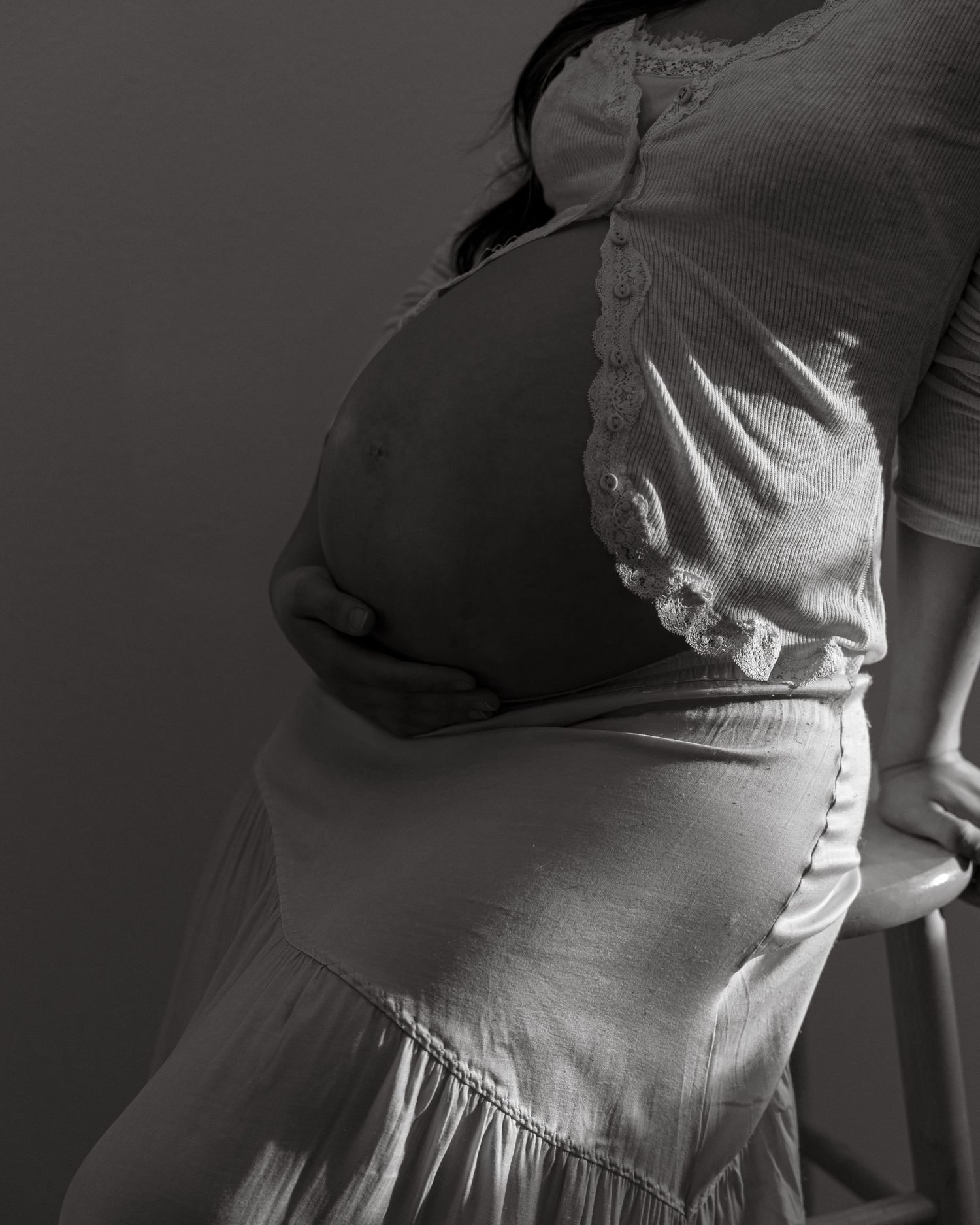 Black and white side profile of a pregnant belly in a flowing dress.