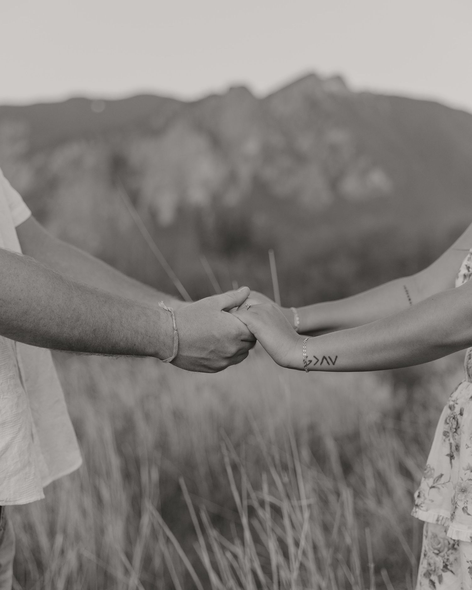 Close-up of two hands holding with mountains in background and tattoo visible.